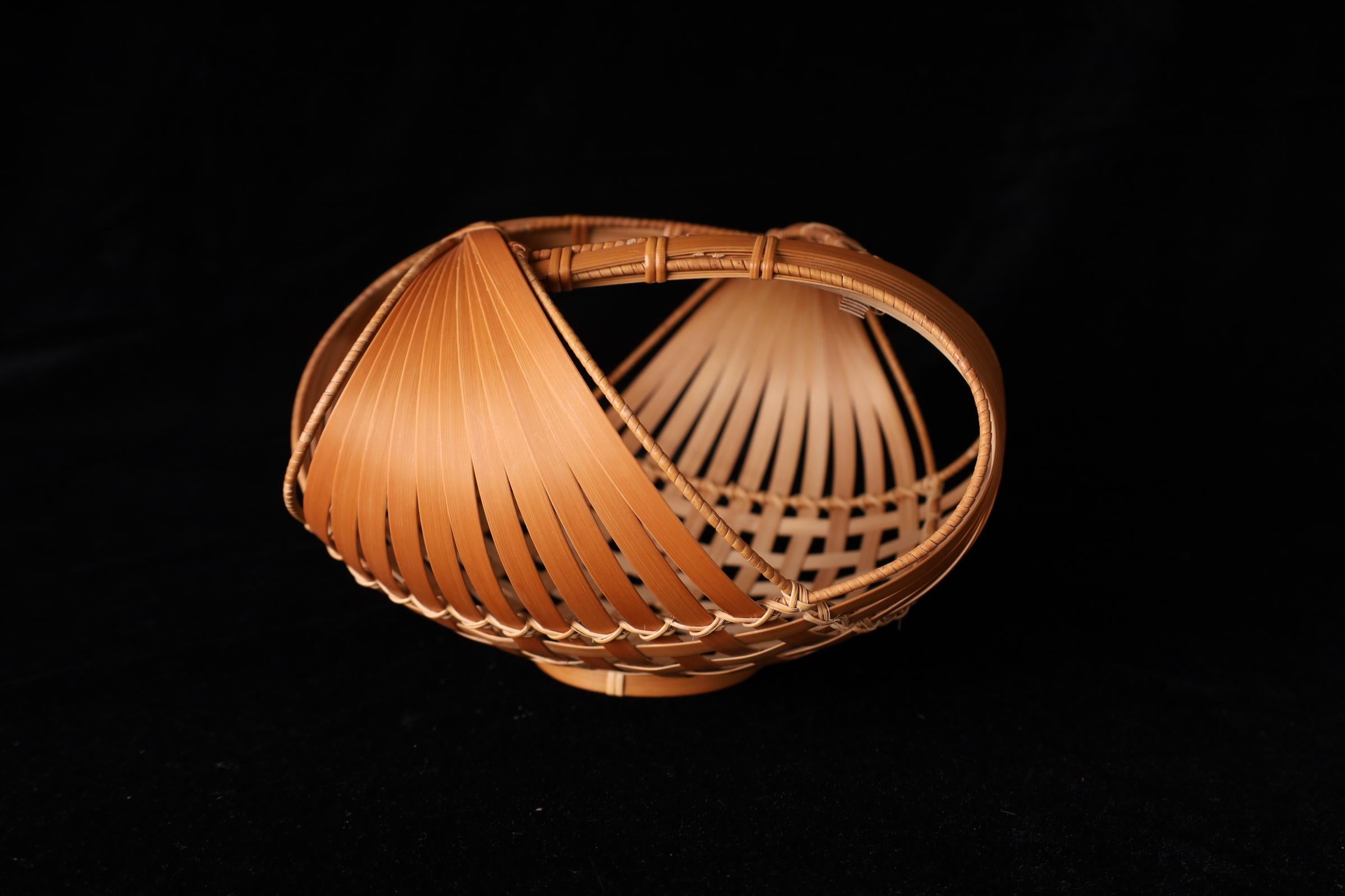 Cesto di fiori di bambù attorcigliato del periodo Showa giapponese
Dimensioni: H. H. 13 cm × L. 21 cm × P. 21 cm

Questo cesto scultoreo in bambù giapponese presenta un dinamico intreccio a spirale, con ampie strisce di bambù spaccate e strettamente