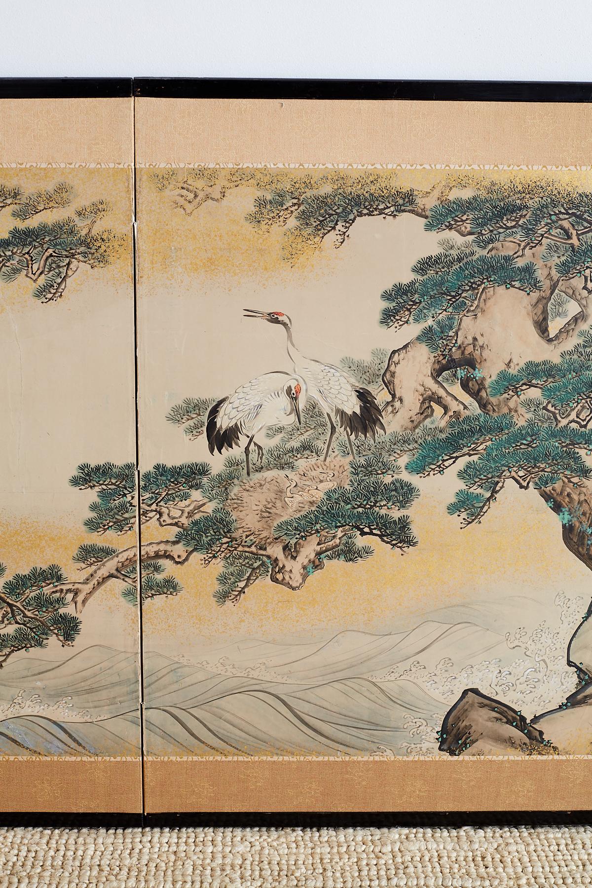 Stunning Japanese Showa period two panel screen depicting red-crowned cranes in an ancient pine tree over crashing waves. Colorful green pigments with later gold leaf specks accenting the entire scene. Signed and sealed on bottom right and set in an