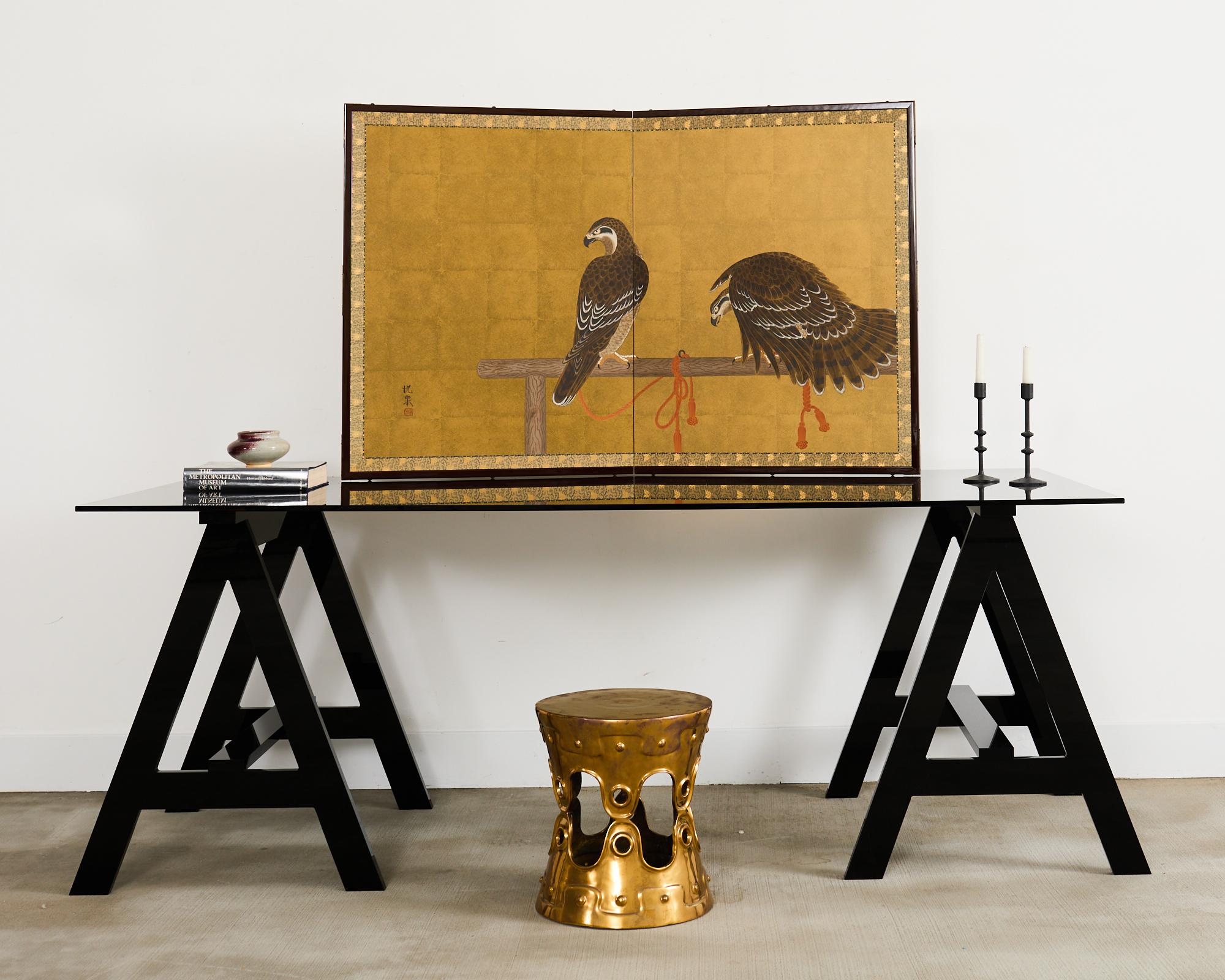 Captivating Japanese Showa period two-panel folding byobu screen featuring a pair of hawks or birds or prey tethered to a wooden perch. The painting has ink and natural colored pigments over a dramatic gilt background. Beautifully painted with