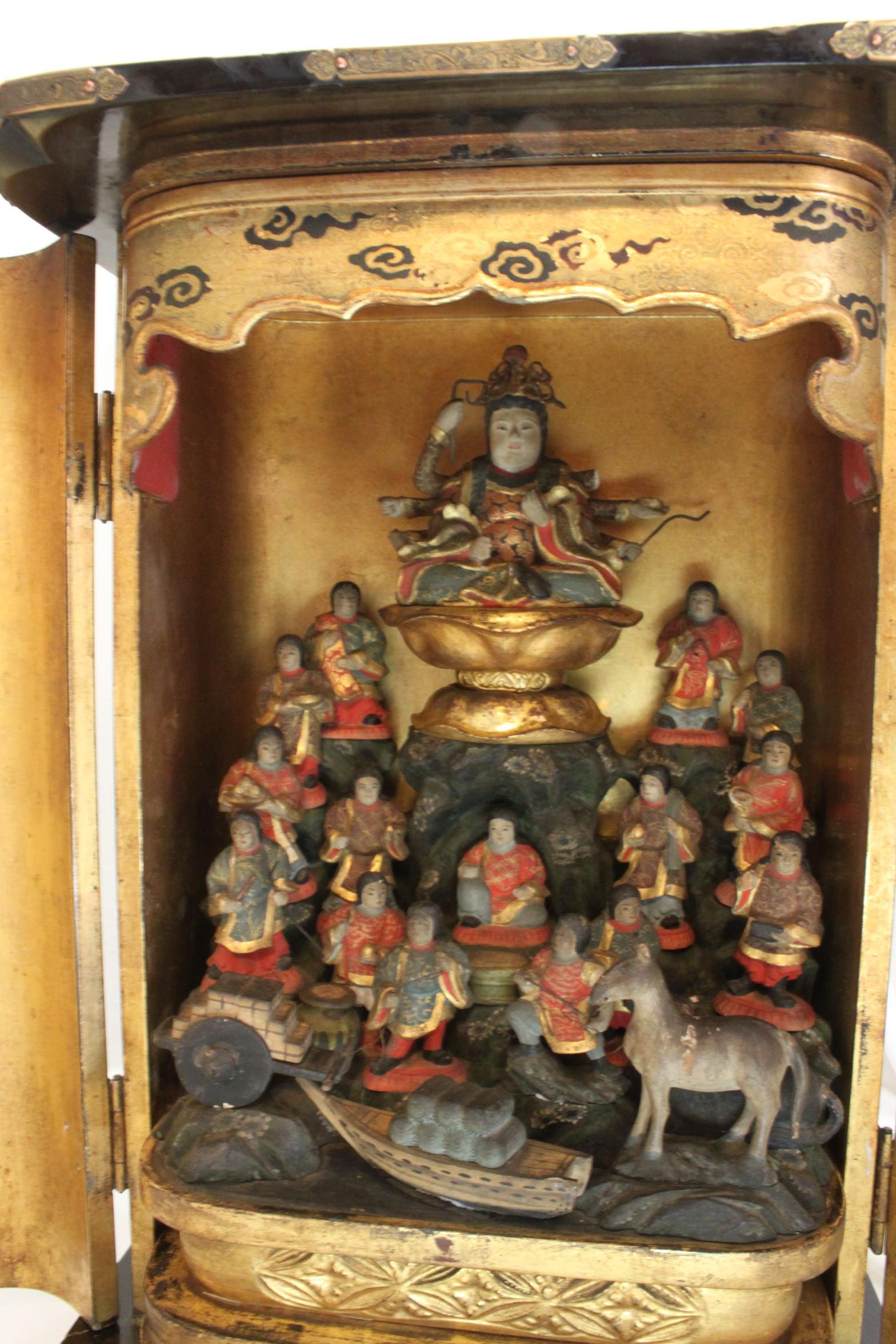 This Japanese travelling shrine or zushi is presided over by an eight armed goddess seated on a lotus throne and beneath her are fifteen figures, all painted and gilded, with some carrying offerings. There is also a horse and a cart and boat laden