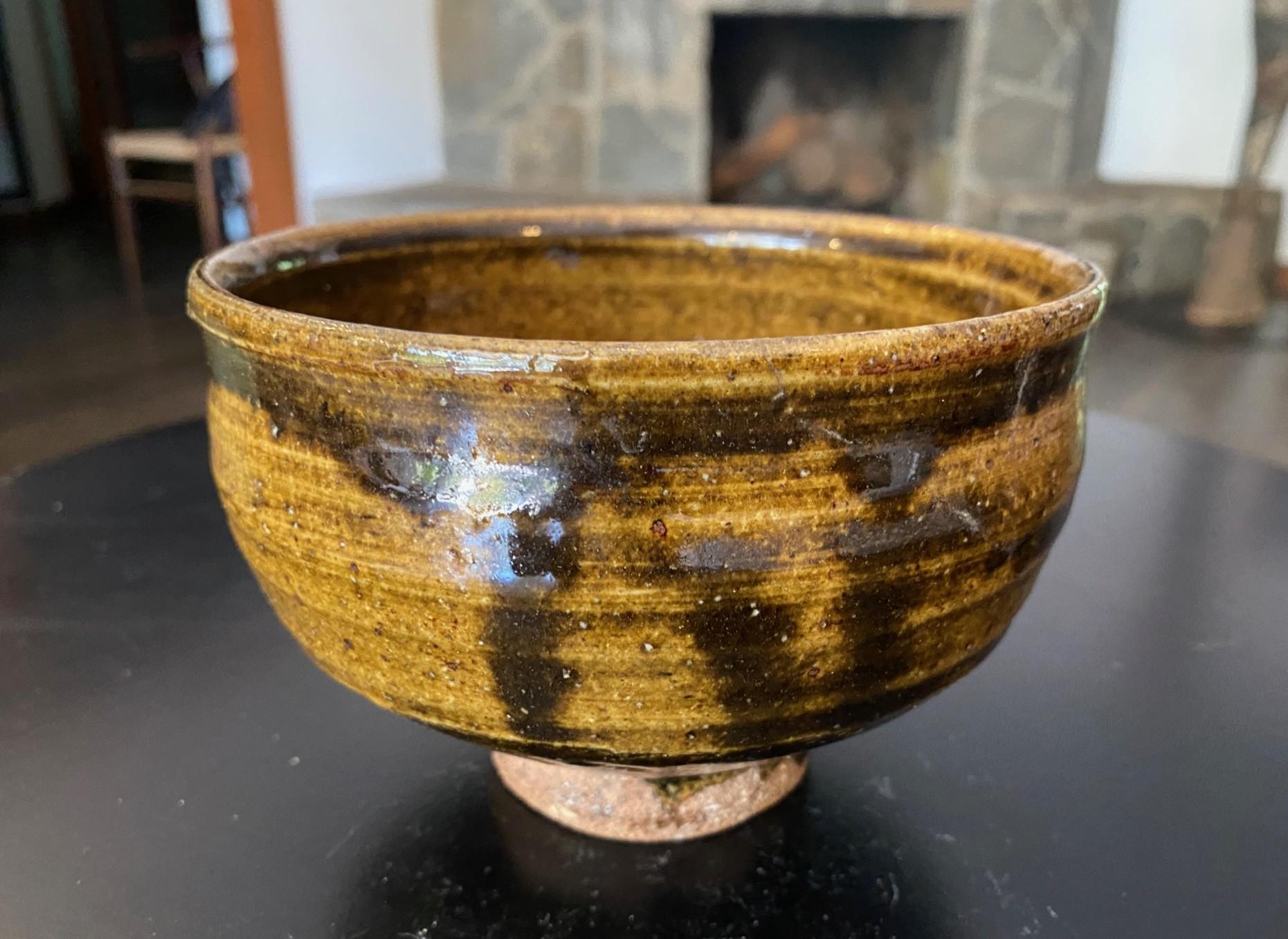 A gorgeous tenmoku drip glazed Japanese Chawan tea bowl that features a mix of shifting colors, glazes and textures.  The piece radiates in the light and is very reminiscent of work that famed British potter Bernard Leach did with Shoji Hamada