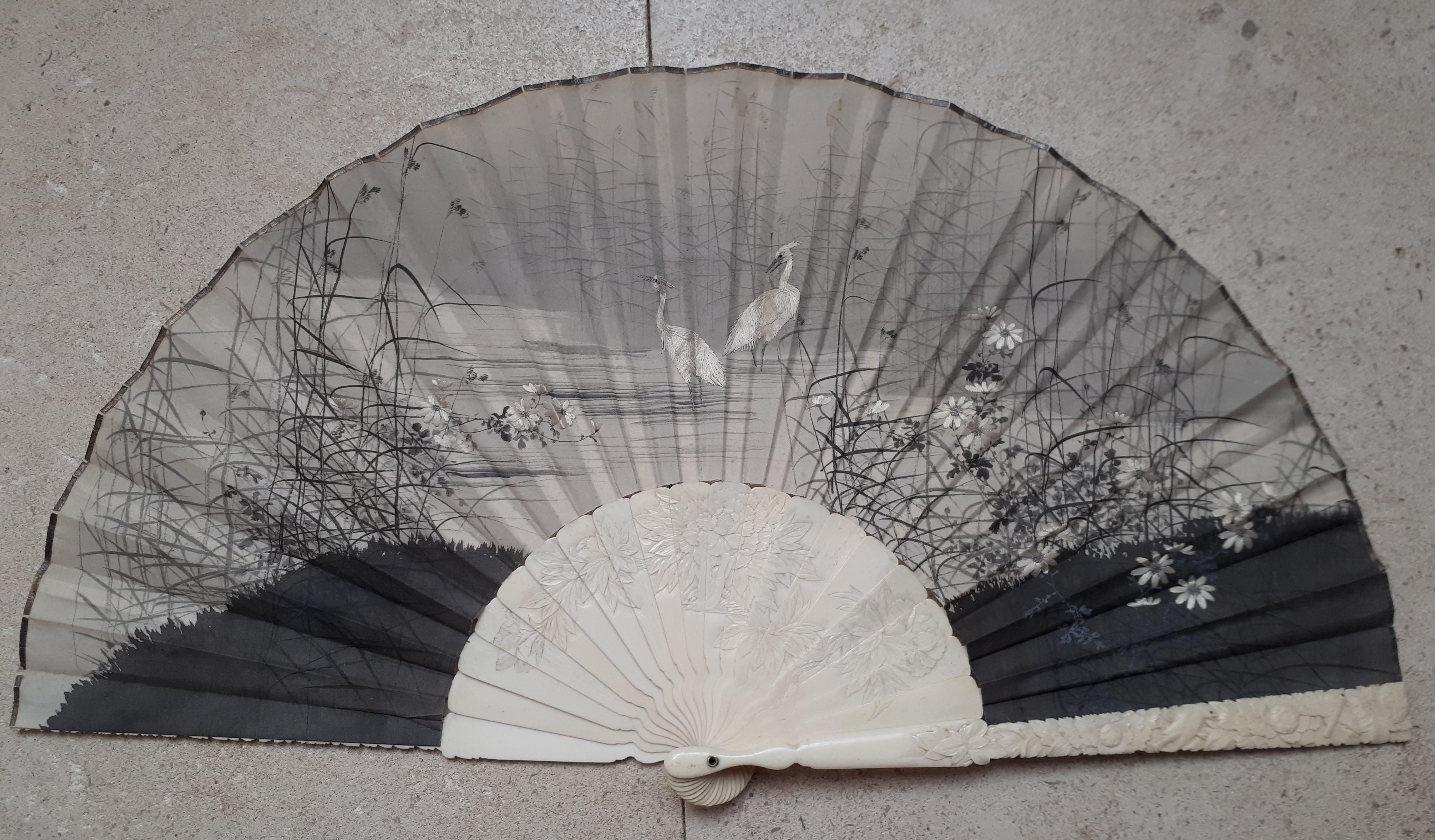 Precious silk fan painted with ink and embroidered, decorated with cranes in a lake landscape. The strands are in finely carved bone decorated with peonies.
Gold signature on the reverse.
Japan, late 19th century.