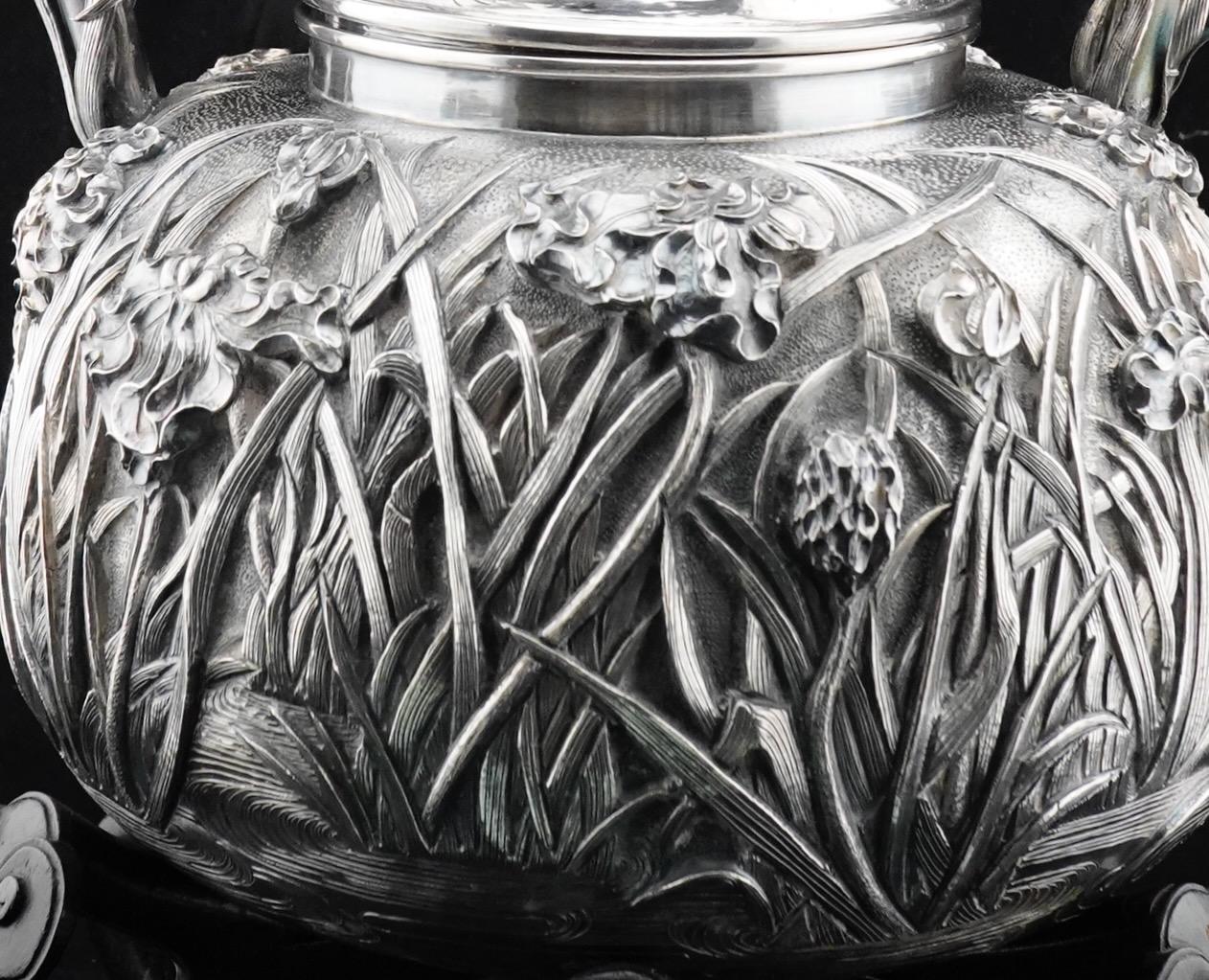 Tetera japonesa de plata Meiji, muy repujada a mano con iris. Elementos fundidos aplicados alrededor del mango. Viene con un soporte de madera personalizado, decorado con hongos lingzi. La tetera está marcada
para la plata pura, fabricante Konoike.