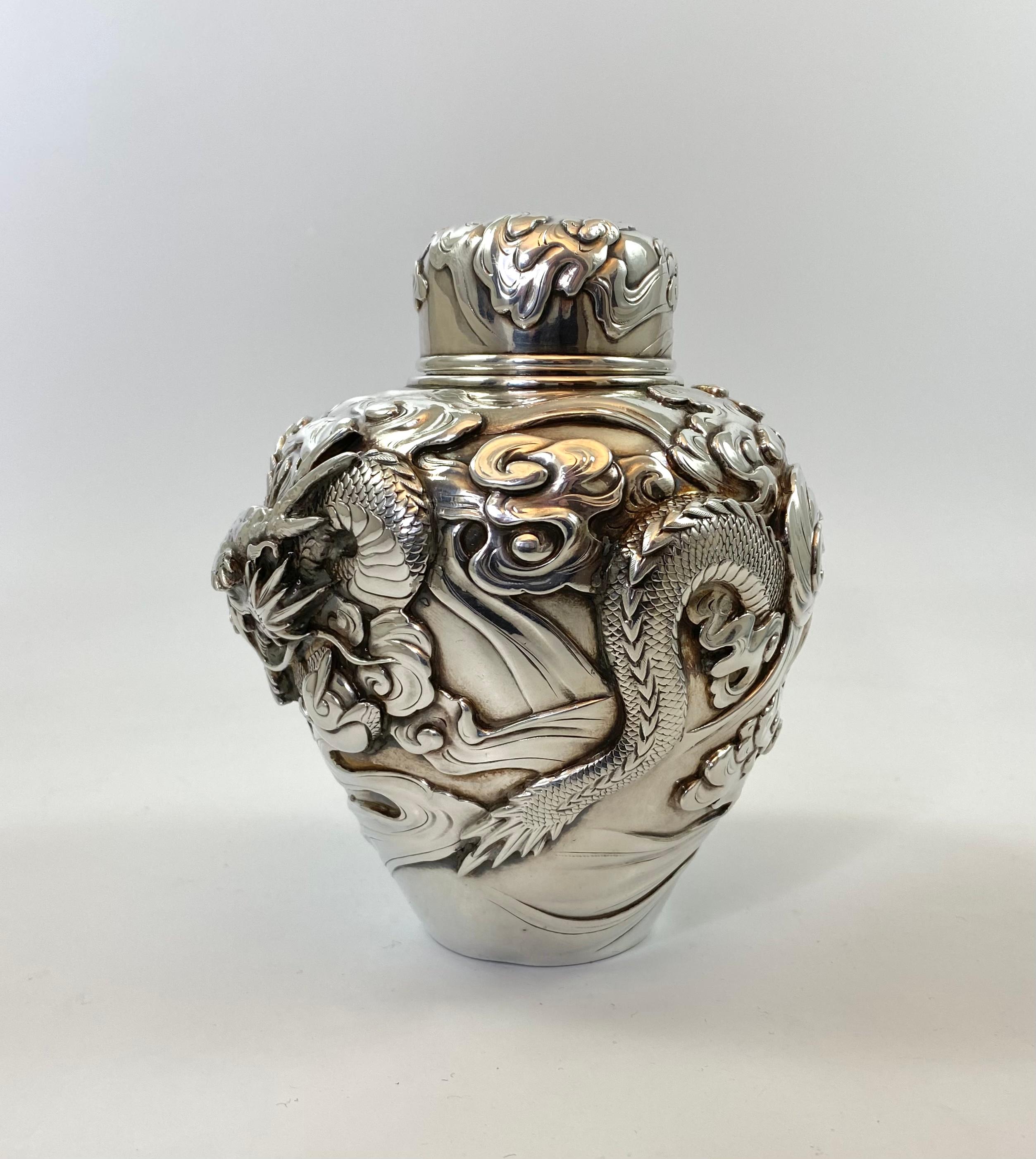 A fine Japanese solid silver tea caddy or natsume, c.1890. Meiji Period. The body, finely cast in heavy relief, and chased, with a sinuous dragon grasping the Pearl of Wisdom, whilst flying above a raging sea.
The cover decorated with further