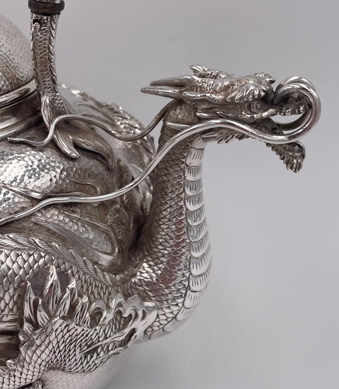 A Japanese silver tea kettle with dragon spout and embossed dragon around the body. The handle is formed of two entwined dragons.