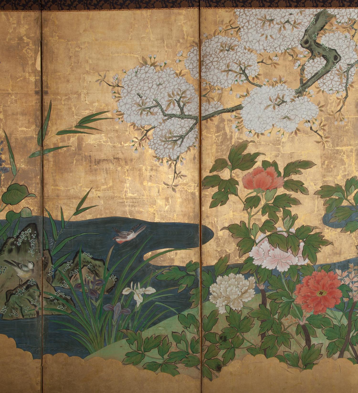 Kano School painting of spring landscape on a river bed, with irises, peonies, lilies, young bamboo and small birds. Mineral pigments and heavy gold leaf on mulberry paper with silk brocade border.
