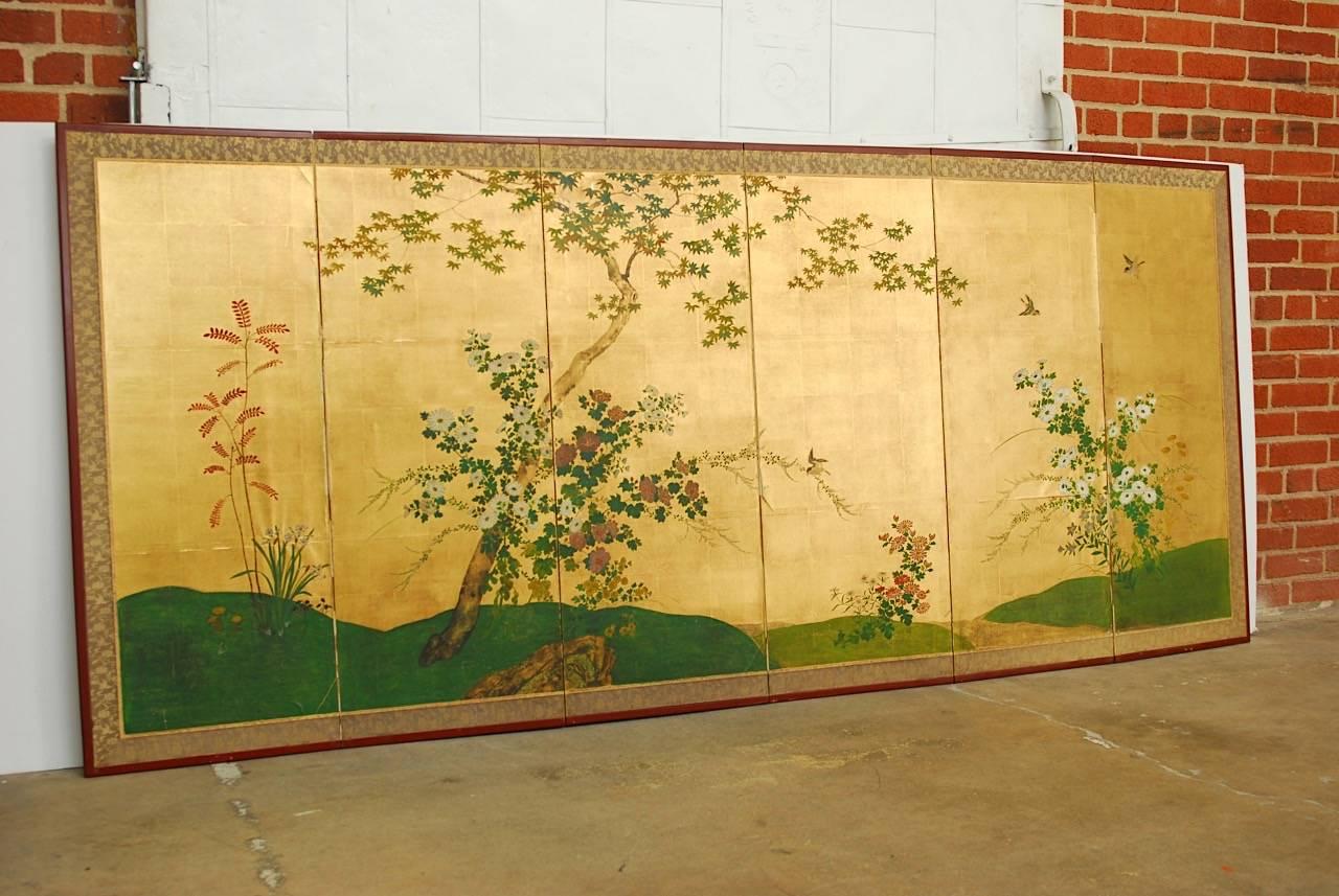 Large Japanese six-panel screen depicting spring blooms of flowers and birds hand-painted on gold leaf squares. This late Meiji period screen is colorful and showcases the intricate details of birds. The chrysanthemums featured on the screen are