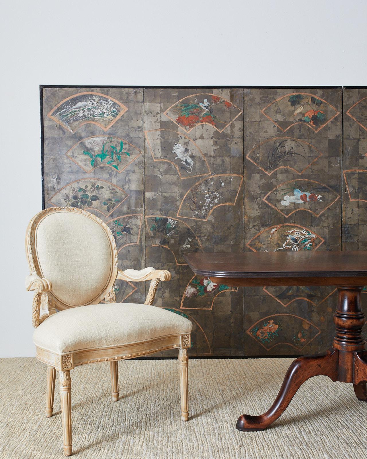 Large scale dramatic Japanese late 19th-early 20th century Meiji screen depicting numerous beautifully painted fans over a silver leaf square background. Originally a six-panel screen now conjoined into a large two-panel screen. The painted fans are