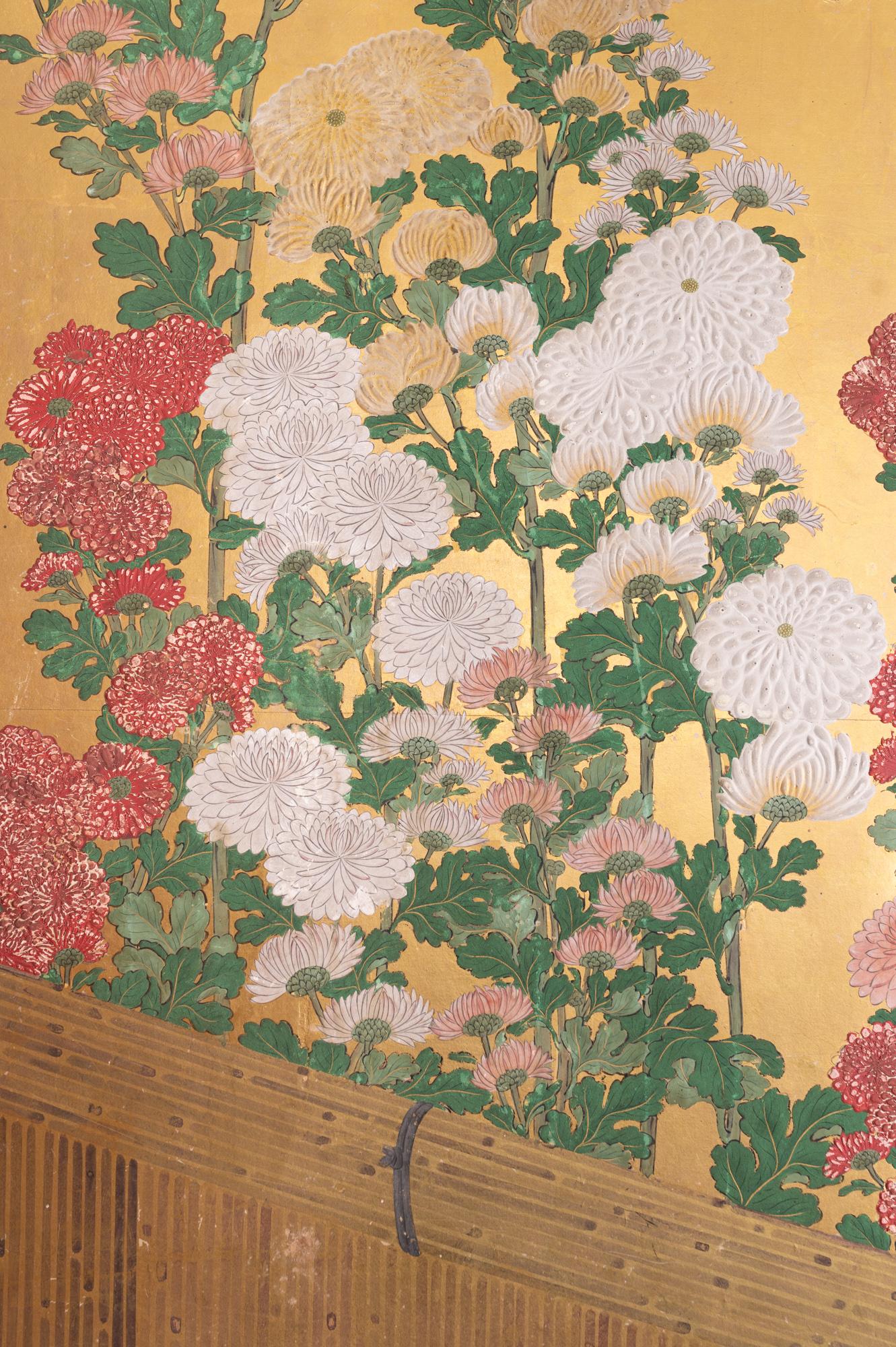 Edo period (18th century) painting of a flowing array of various types of chrysanthemums painted on beautifully faceted heavy gold leaf and behind afinely painted fence. Petals of the chrysanthemums are rendered in raised gofun. This screen has the