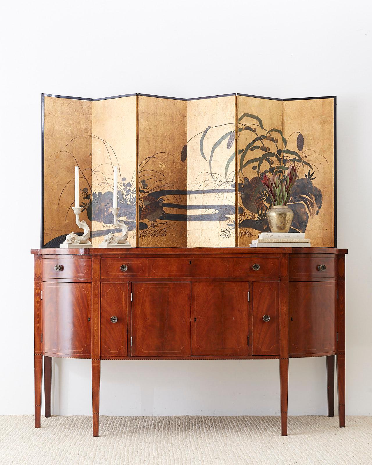 Distinctive Japanese six-panel screen depicting a meandering river landscape with quail among millet grasses and rocks. Painted in the Rimpa school style with ink and color pigments over thick gold leaf squares. Set in a black lacquered wood frame.