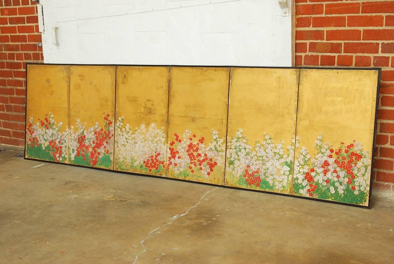 19th century Japanese Meiji six-panel screen featuring colorful red and white spring flowering blossoms on a gold leaf ground. This large screen has a beautiful antique patina with foxing and fading that add to its vintage look. Set in an ebonized