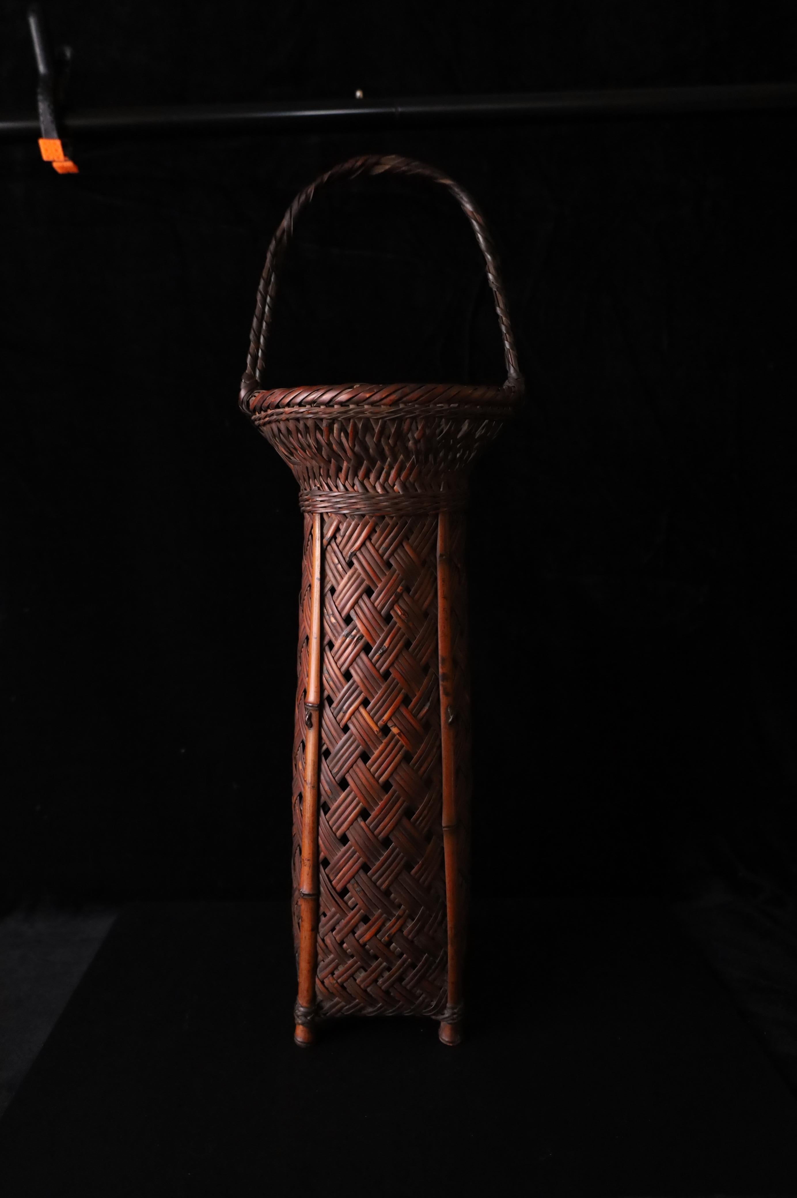A beautifully handwoven Japanese bamboo basket, crafted in the early 20th century for use in ikebana (the art of flower arranging). This tall, narrow form with a rounded rim and twisted handle is both elegant and functional, showing the refined