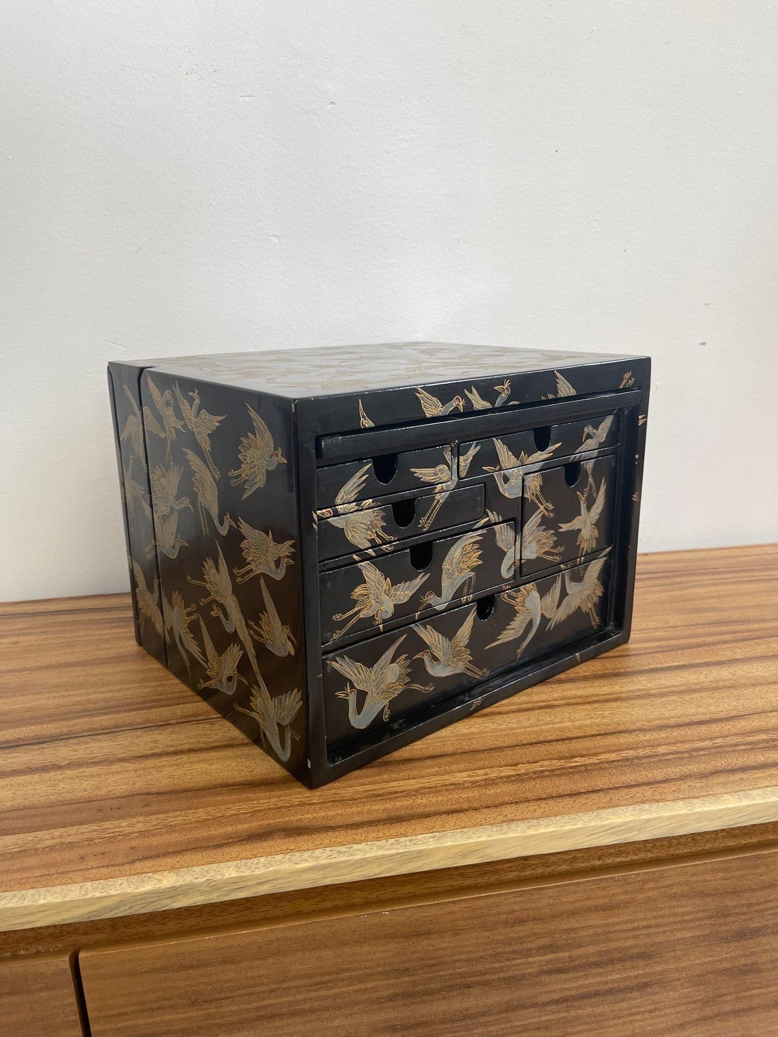 This beautiful piece is covered in crane images, even the inside of the drawers have them. Two compartments for drawers, one revealed through a hinge door and the other through sliding a panel of the exterior box up. The Box is wooden. May be