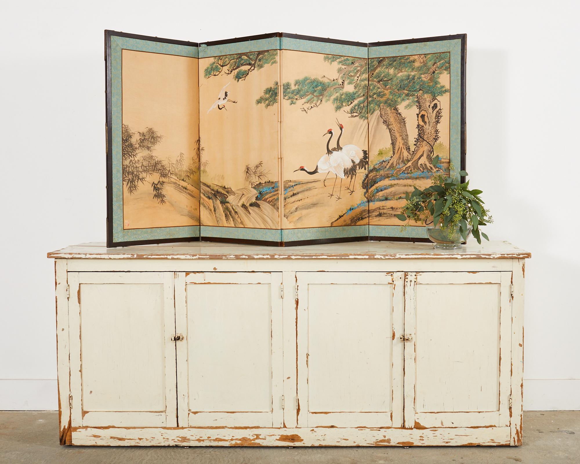 Distinctive Japanese style Showa period four panel folding byobu screen featuring four cranes near ancient pine trees. The beautifully depicted landscape has a stream and bamboo in the background. Ink and vivid color pigments on hand-crafted paper