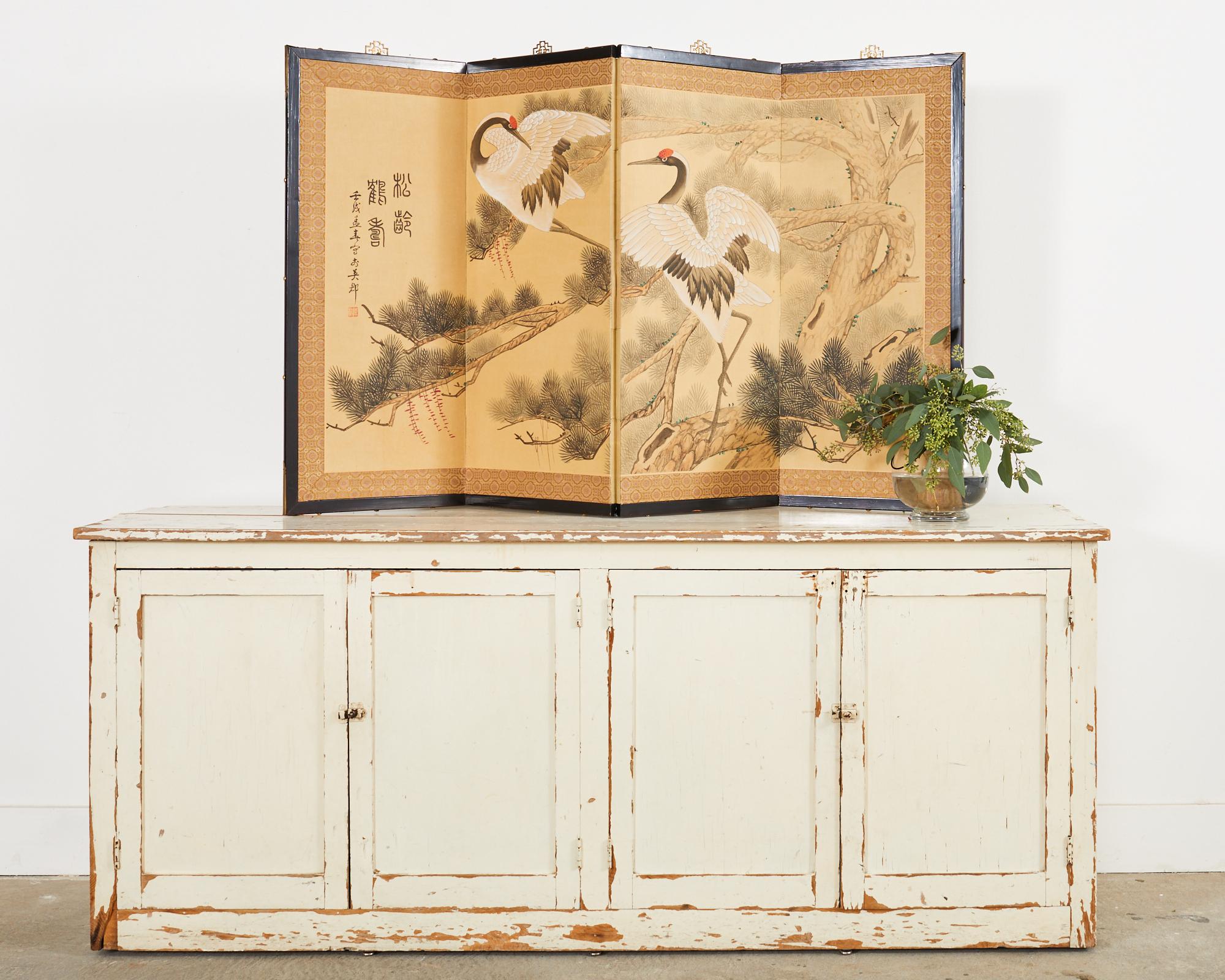 Captivant paravent à quatre panneaux de style japonais byobu du 20e siècle. Le paravent est intitulé pin ancien/grues de longévité et signé sur le côté gauche avec le sceau de l'artiste Ying Jun. L'écran représente deux grues blanches de Mandchourie