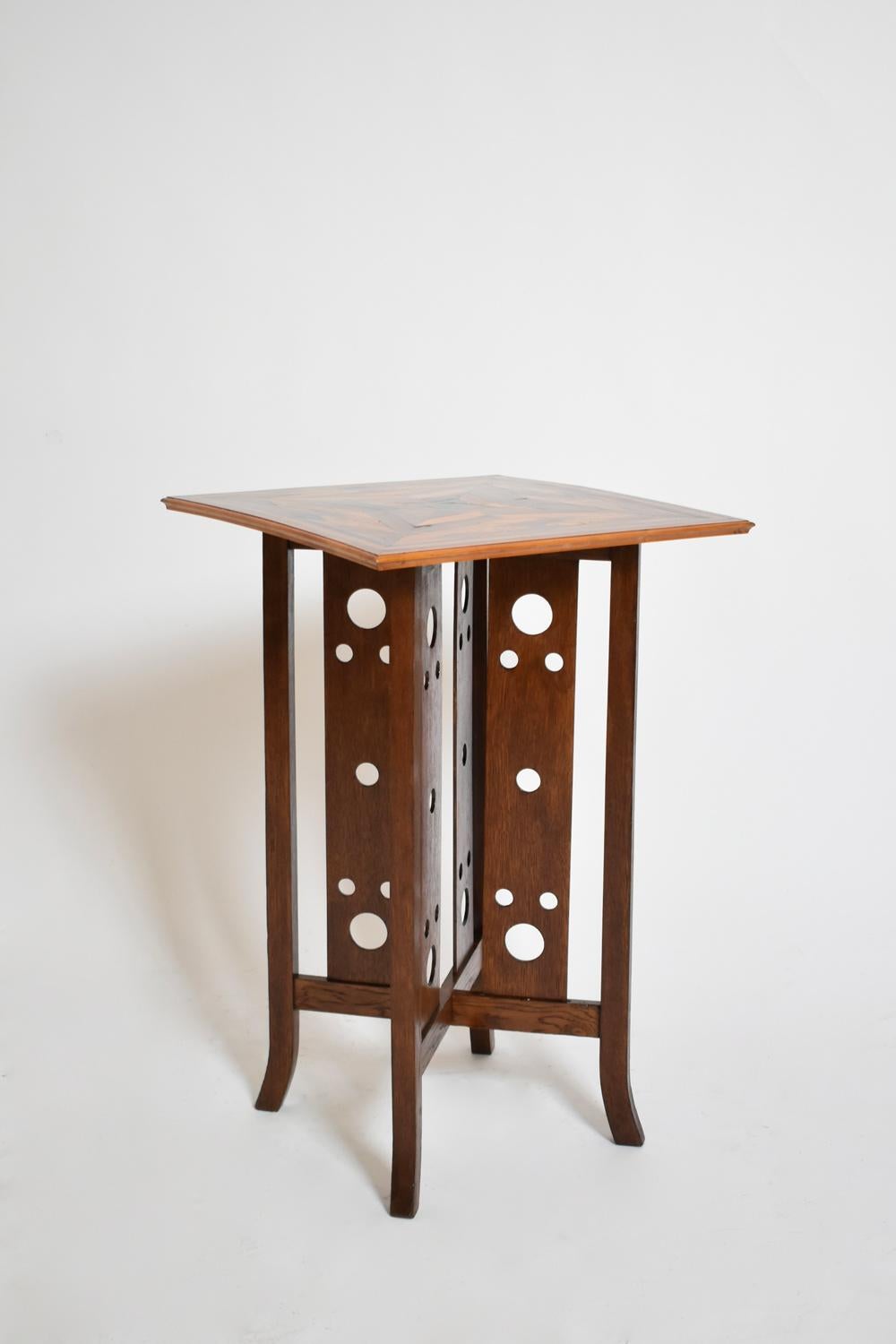 Tavolo con piedistallo quadrato che poggia su quattro montanti centrali decorati con dischi e che sostiene un piano quadrato ornato da un motivo geometrico arlecchino realizzato con intarsio di essenze di legno e guscio di tartaruga, nello stile del