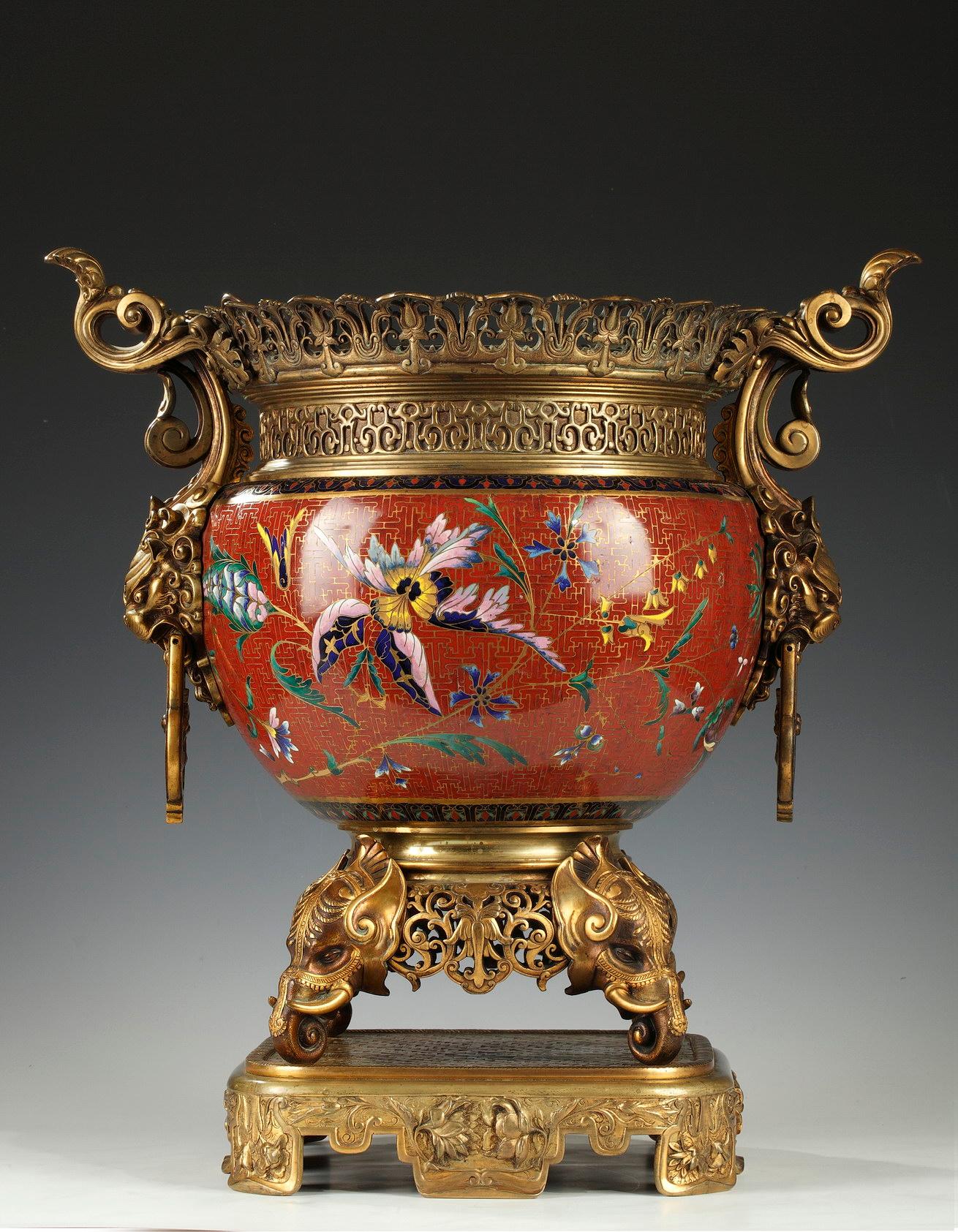 Large planter decorated on the belly with a rotating decoration of polychrome flowers and geometric patterns in cloisonné enamel on a red background. It is inserted in an important patinated and gilded bronze frame composed of openwork friezes on
