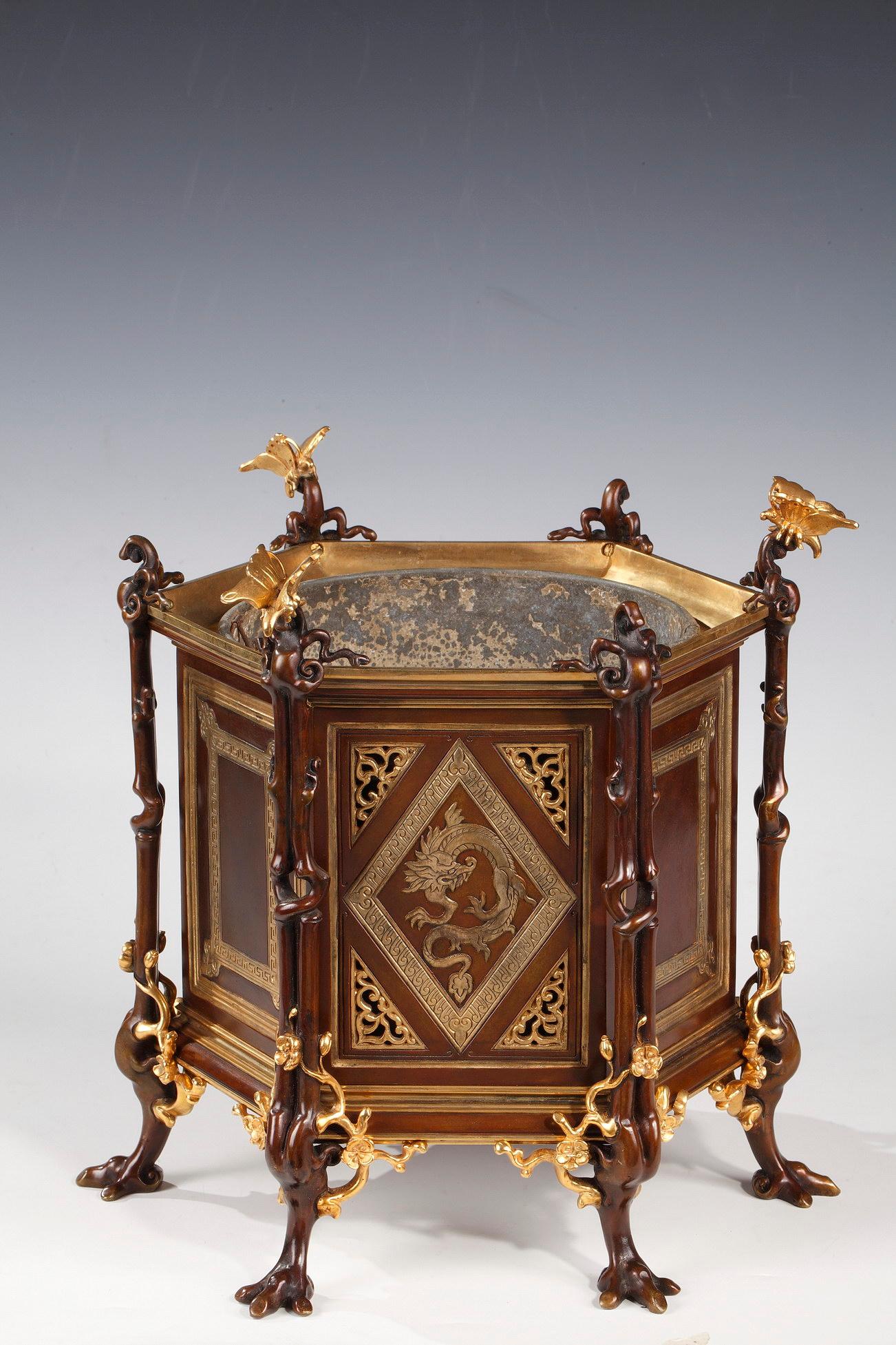 Signed H.P for Henri Pannier.

Lovely hexagonal shaped planter in patinated bronze with gold highlights. Adorned on three sides with a dragon framed by a rhombus frieze on an openwork background.
It is framed by six uprights showing branches