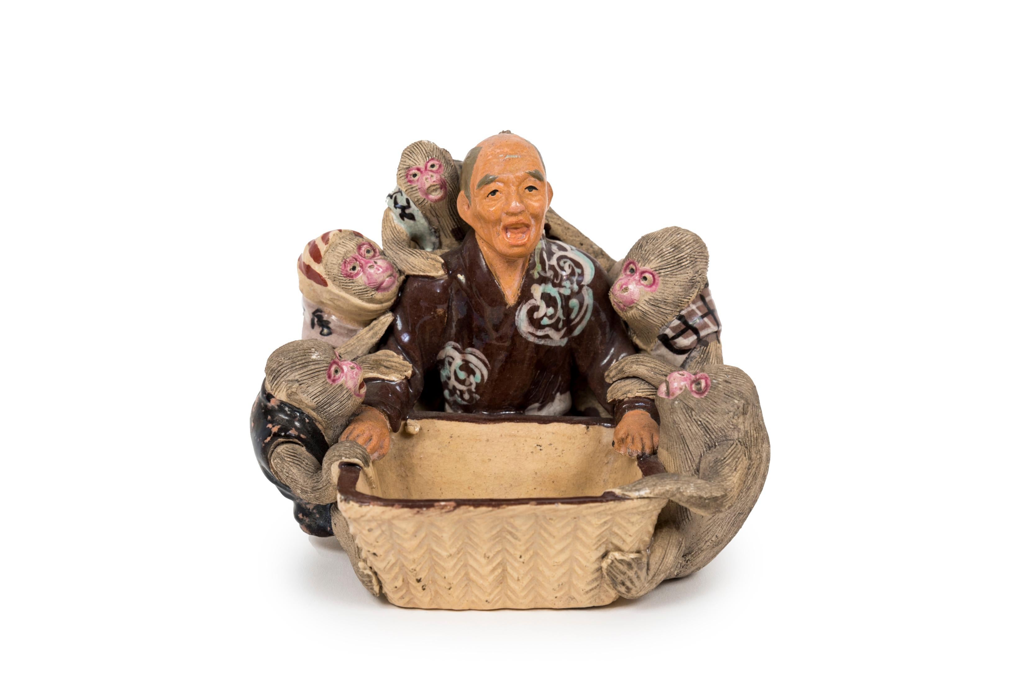 Sculpture polychrome en grès de Sumida-gawa, également appelée Sumida-yaki, représentant un vieil homme entouré de cinq singes devant un panier contenant deux noix. Vêtements et panier émaillés. La figure du singe avec des pêches de longévité est