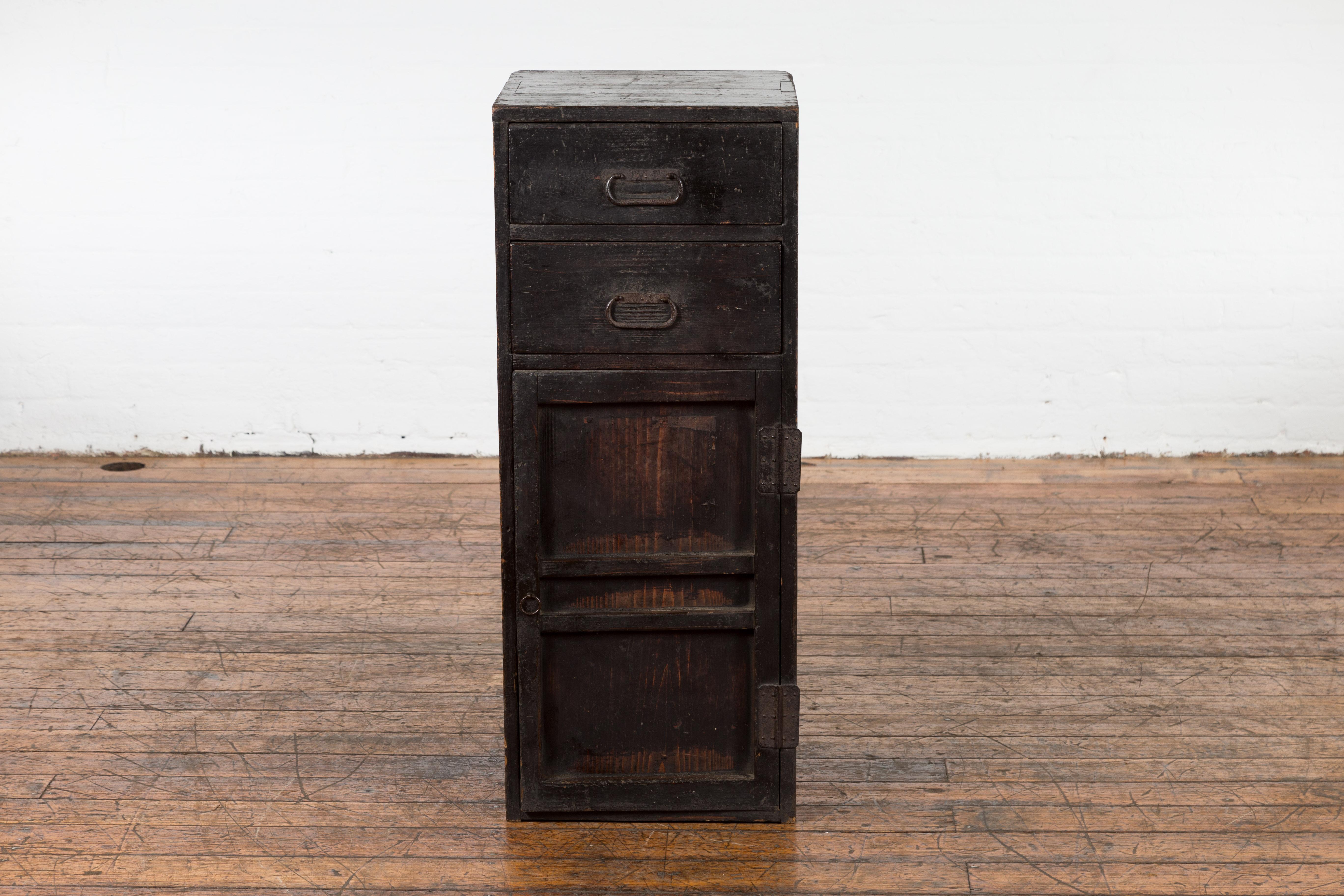 An antique Japanese Taisho period dark brown lacquered side cabinet from the early 20th century with two drawers, single door, inner shelves, metal hardware and weathered appearance. Capturing the essence of the early 20th-century Japanese Taisho