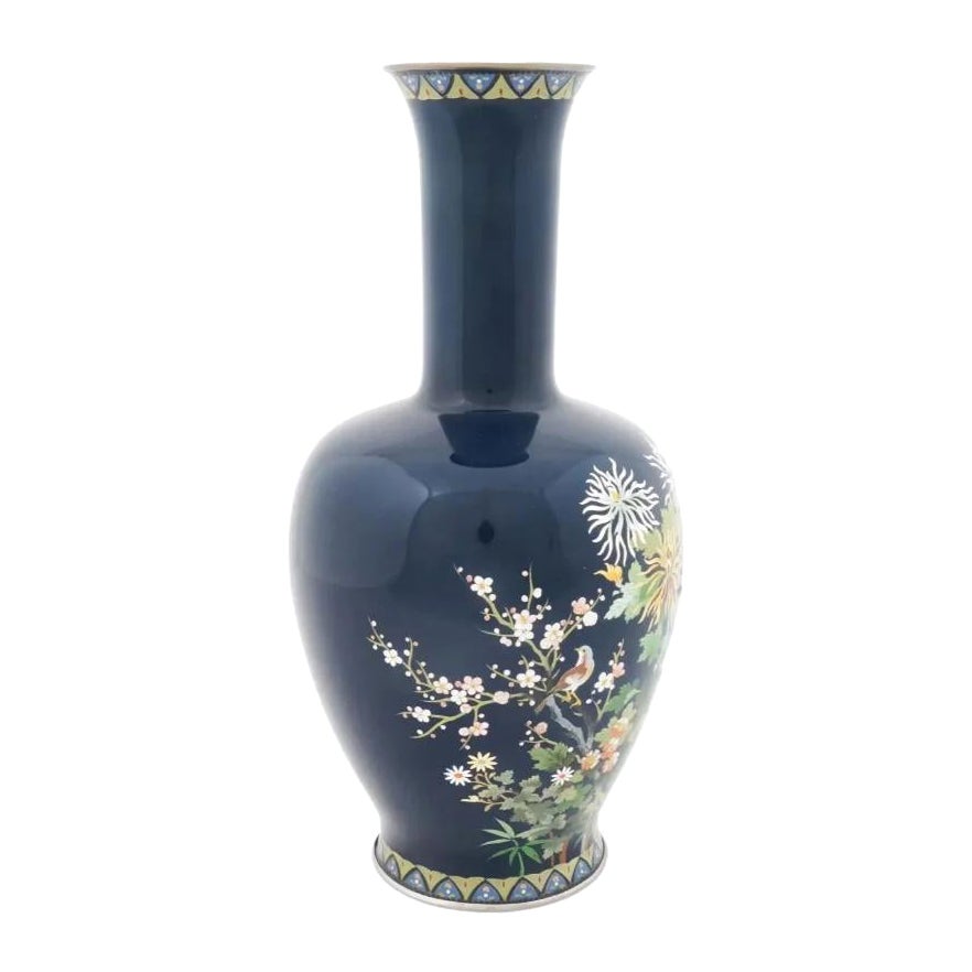 Jarrón japonés de esmalte cloisonné del Periodo Taisho, 1912-1926, con fondo azul oscuro brillante y decorado con un motivo policromo tradicional que representa un pájaro entre flores. Marcado en la base: Hecho en Japón y tiene una marca de fábrica