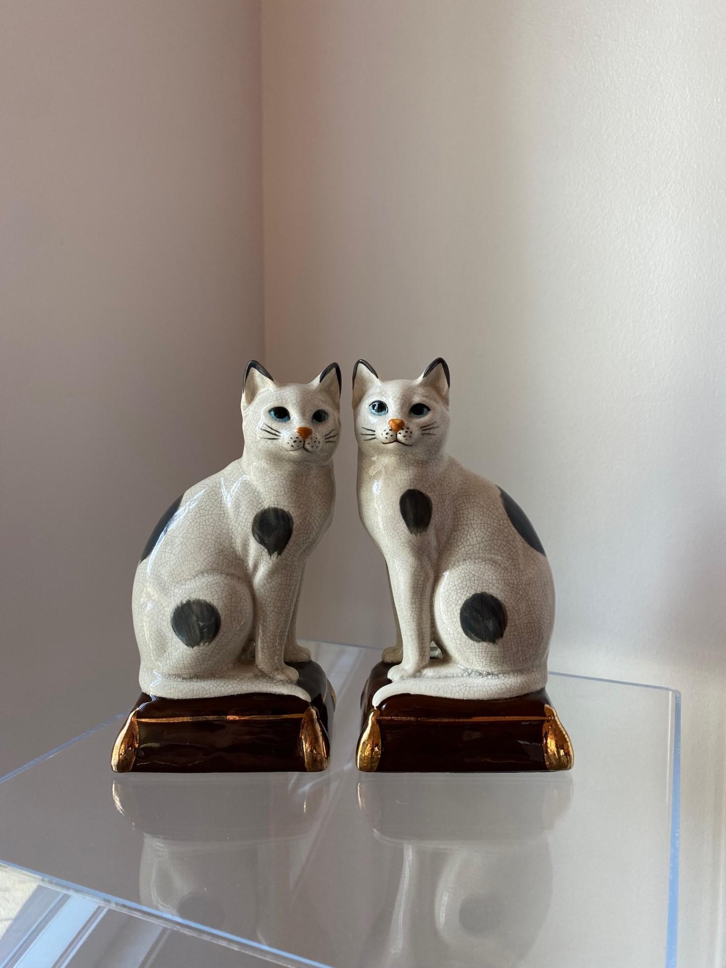 Fabulous pair of porcelain Takahashi cats in white with black blotches sitting on cushions with gold trim and tassels. Underneath the protective felt pad is a hole which the company purposely made so that pebbles or sand could be filled to add