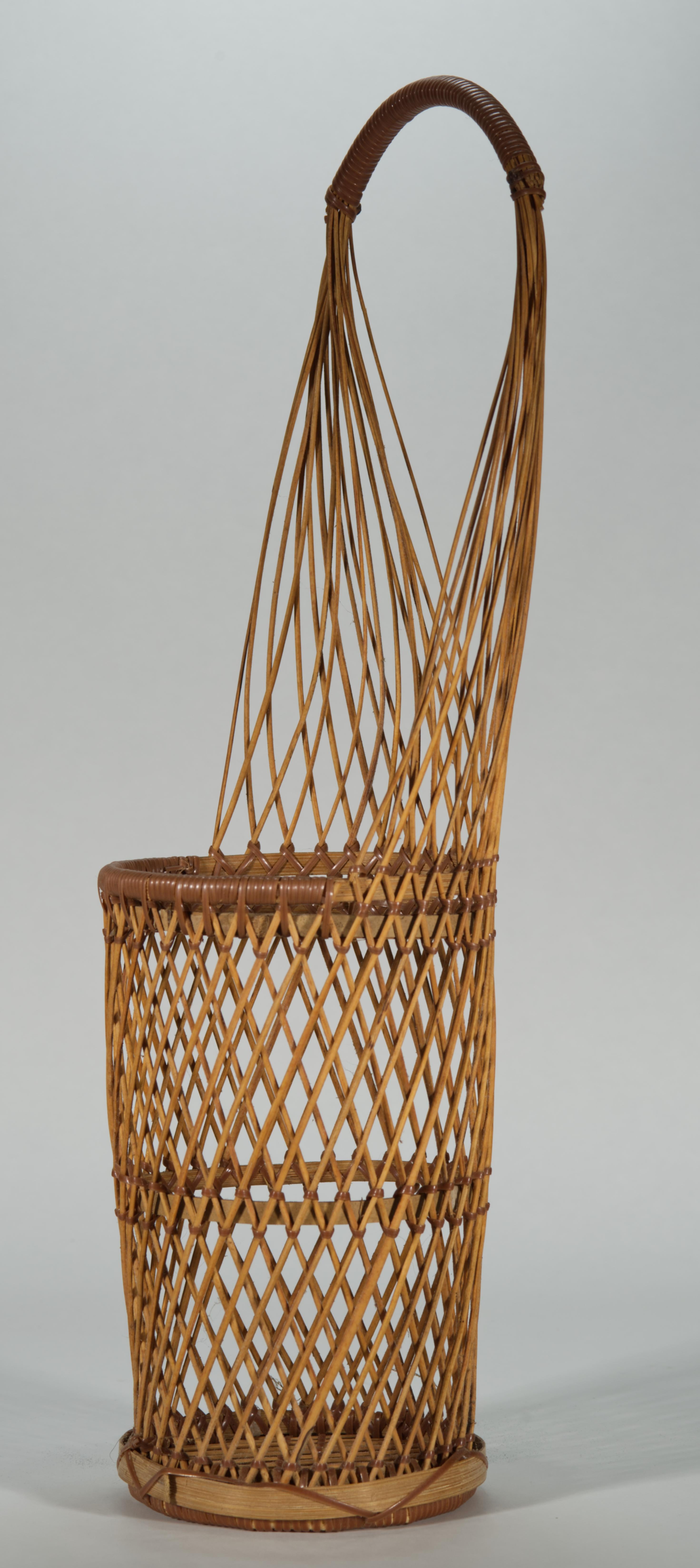 Le panier Vintage By Ikebana en bambou présente une forme cylindrique haute avec une poignée arrondie proéminente. Le panier est tressé avec de fines bandes de bambou rondes qui sont fixées avec des fibres marron clair, ajoutant stabilité et