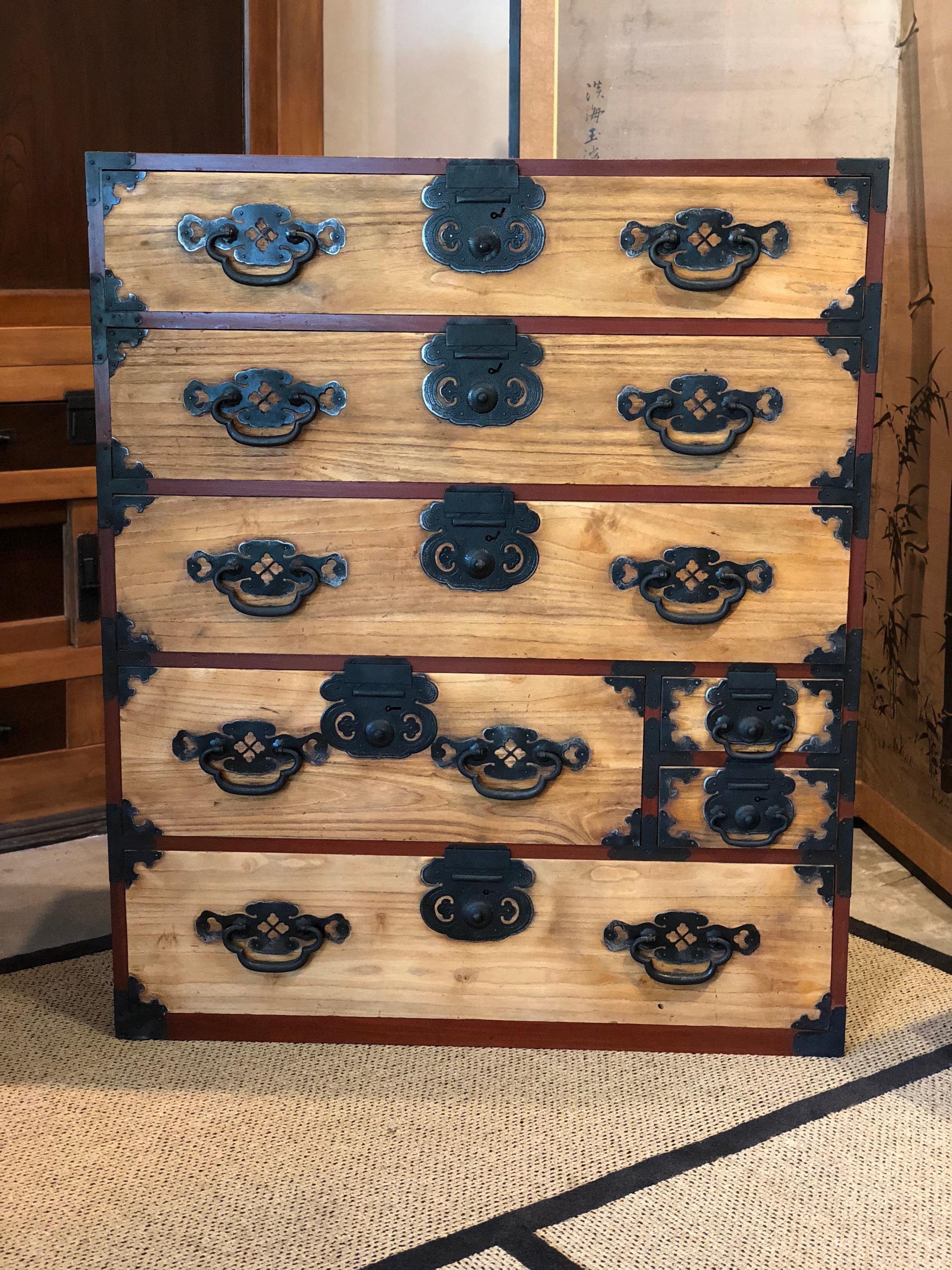 Japanese tansu chest constructed of kiri with large iron handles and massive iron lock plates with a distinctive motif. This is a unique tansu because its casing is a red brown lacquer giving it a stately look. Elongate escutcheon are gracefully