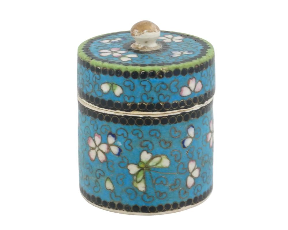 Jarra o caja de jengibre japonesa cubierta de esmalte Totai sobre porcelana. La vajilla, de forma cilíndrica, está esmaltada con motivos policromos florales, de follaje y geométricos sobre fondo turquesa, realizados con la técnica cloisonné. La tapa