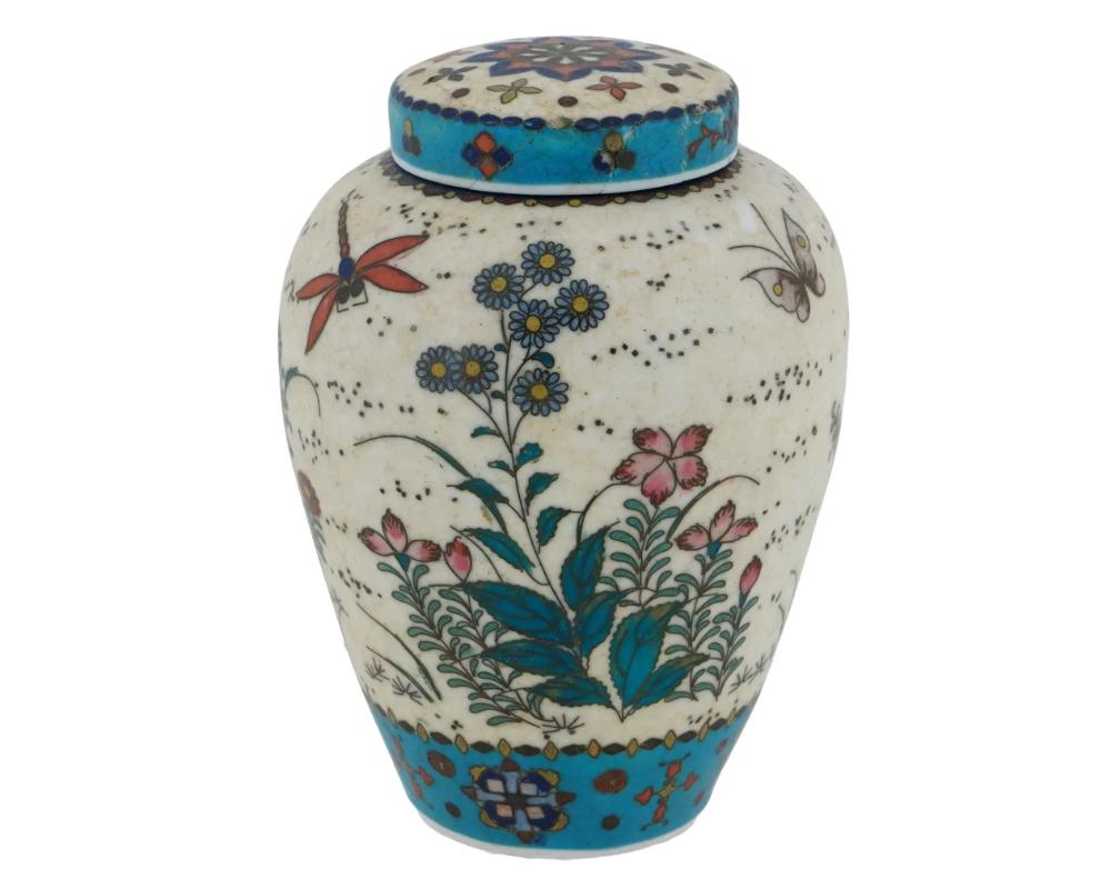 A Japanese covered Totai enamel on porcelain ginger jar. The ware is enameled with polychrome images of blossoming flowers, butterflies, and dragonflies made in the Cloisonne technique. The cover of the ware is made in the same design. The neck and