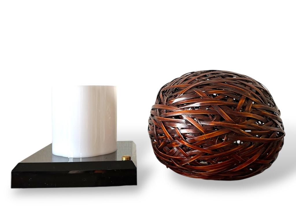 This sculptural Japanese lamp features a handwoven bamboo shade in the form of a perfect sphere, composed of richly stained bamboo strips intricately interlaced in a traditional basketry style. The sphere rests atop a glossy black lacquered wooden