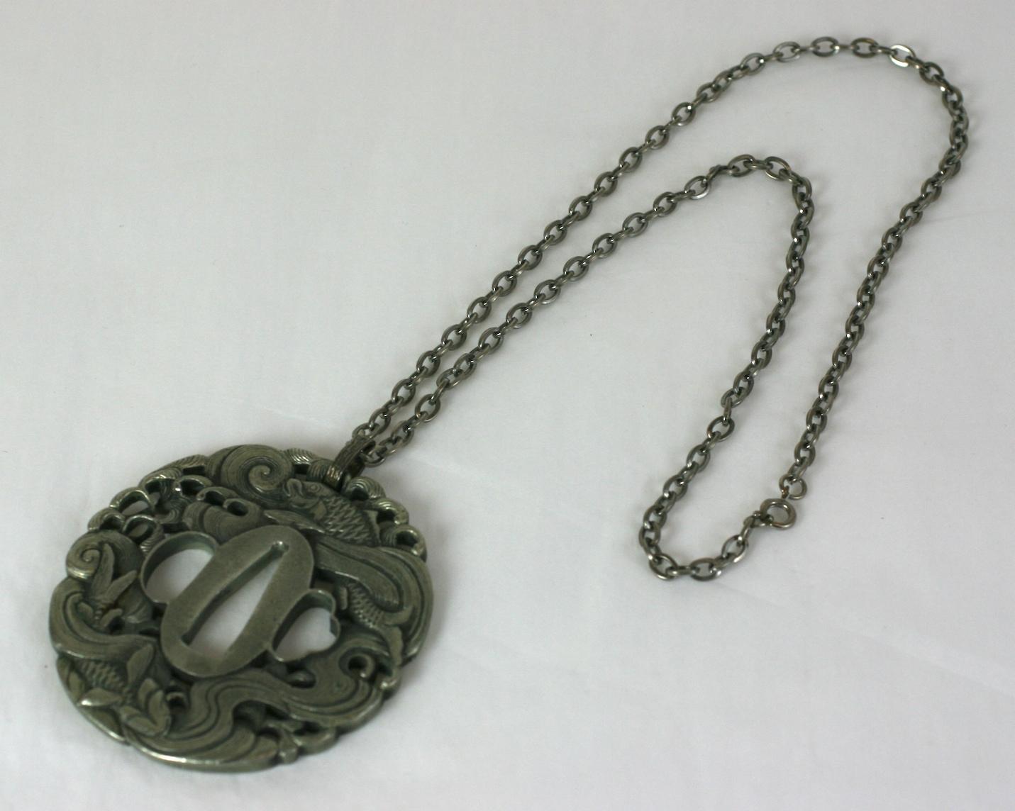 Ciondolo Tsuba giapponese in metallo color argento antico. La tsuba è il guardamano di una spada giapponese. Si tratta di una replica di un pezzo antico realizzato negli Stati Uniti nel 1960 circa.  Condizioni eccellenti. 
Catena 24