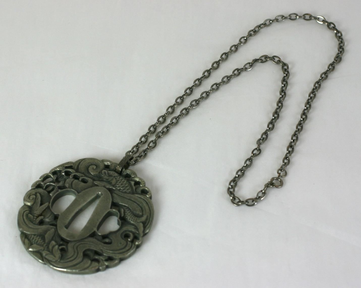 Japanese Tsuba Pendant in antique silver toned metal. A tsuba is the hand guard of a Japanese sword. This is a replica of an antique piece made in the USA circa 1960.  Excellent condition. 
Chain 24