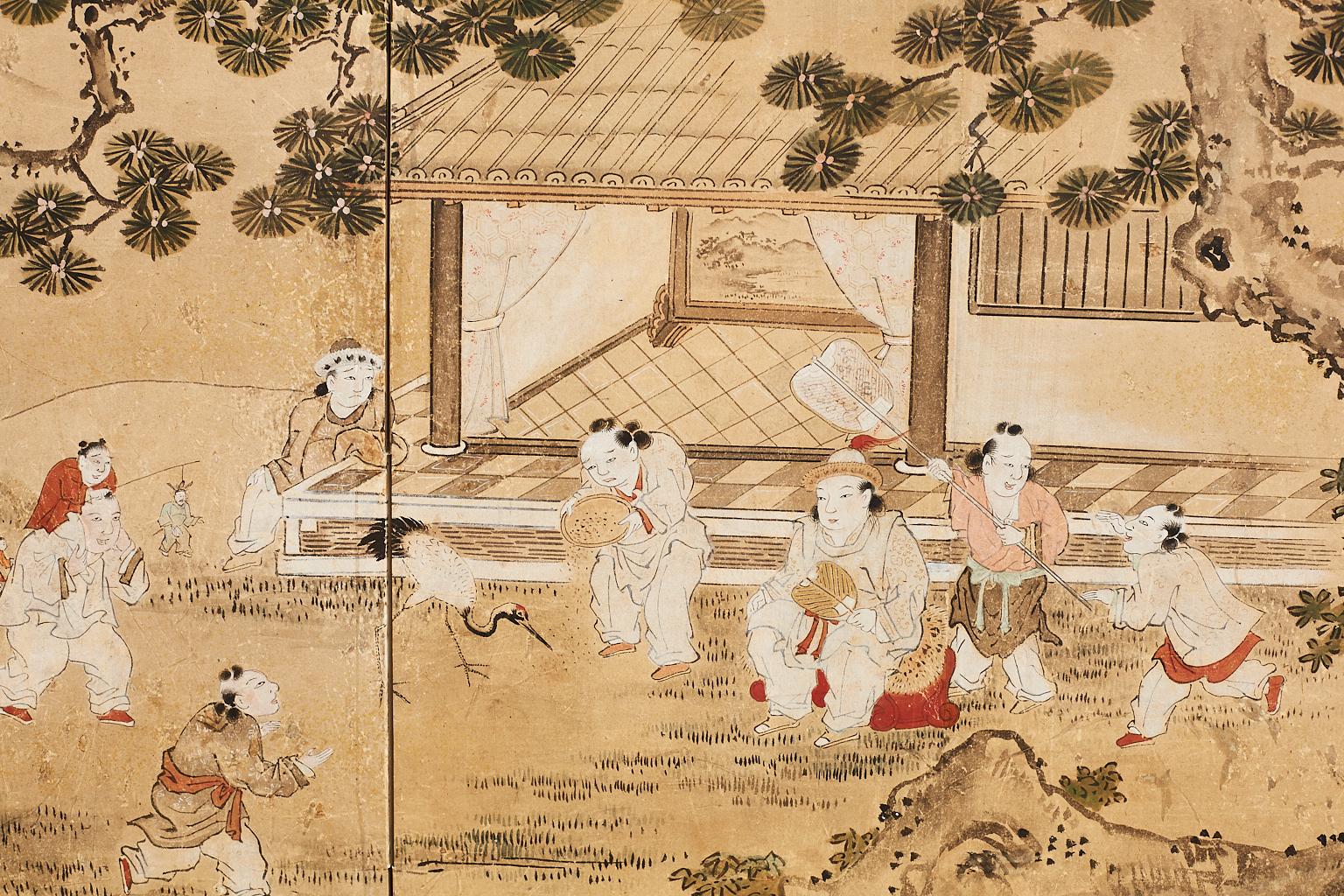 Exquisite Japanese two-panel Meiji period painting made in the Kano school style. Features a lively scene of children playing in a yard under an ancient pine tree near a home. The painting is surrounded by gold leaf clouds and set in a later