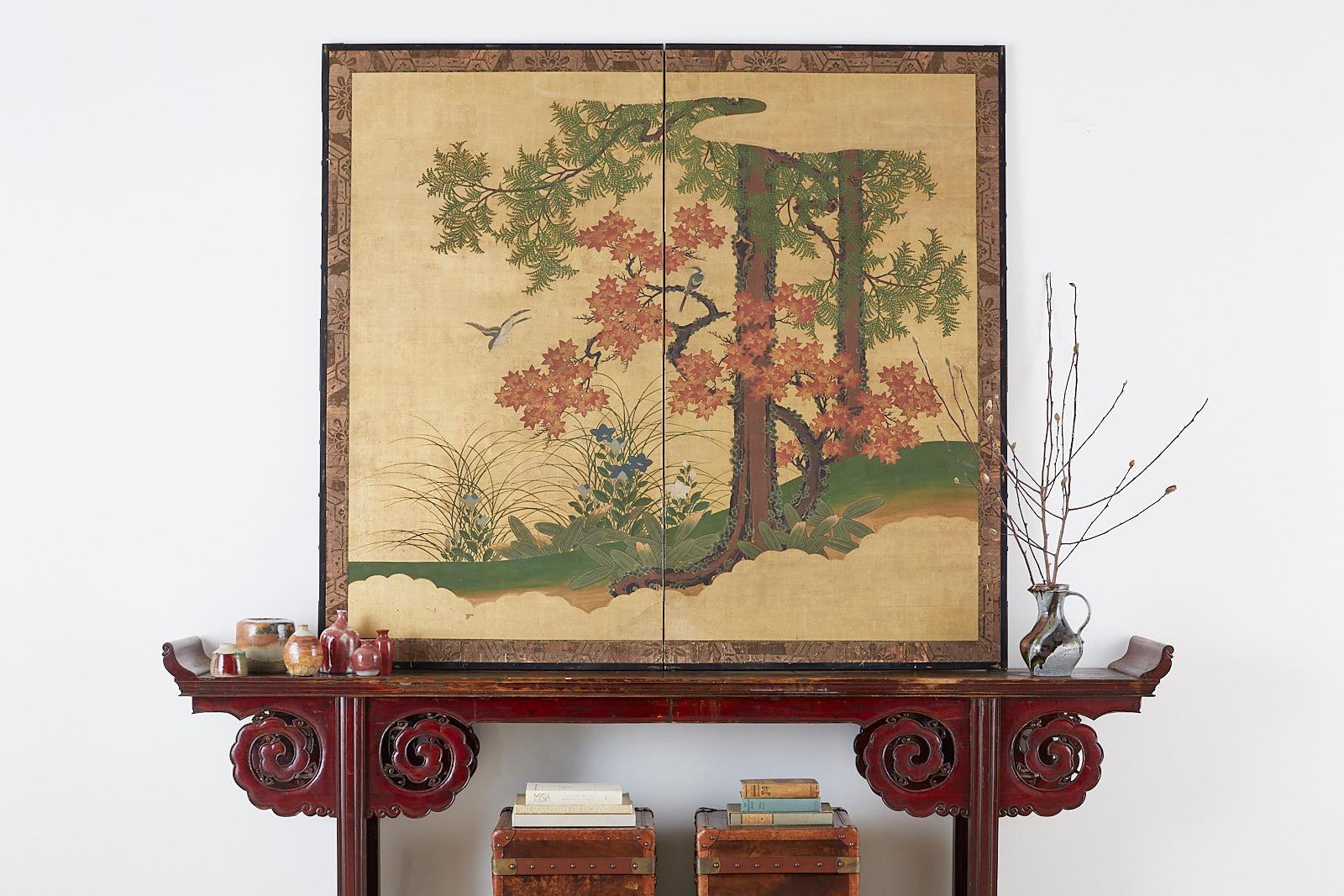 Late 19th century Japanese Meiji period two-panel screen depicting an autumn landscape with Japanese song birds. The screen features a Buddhist pine or Maki tree and a Japanese maple or momiji tree. Painted with ink and color over gold leaf squares