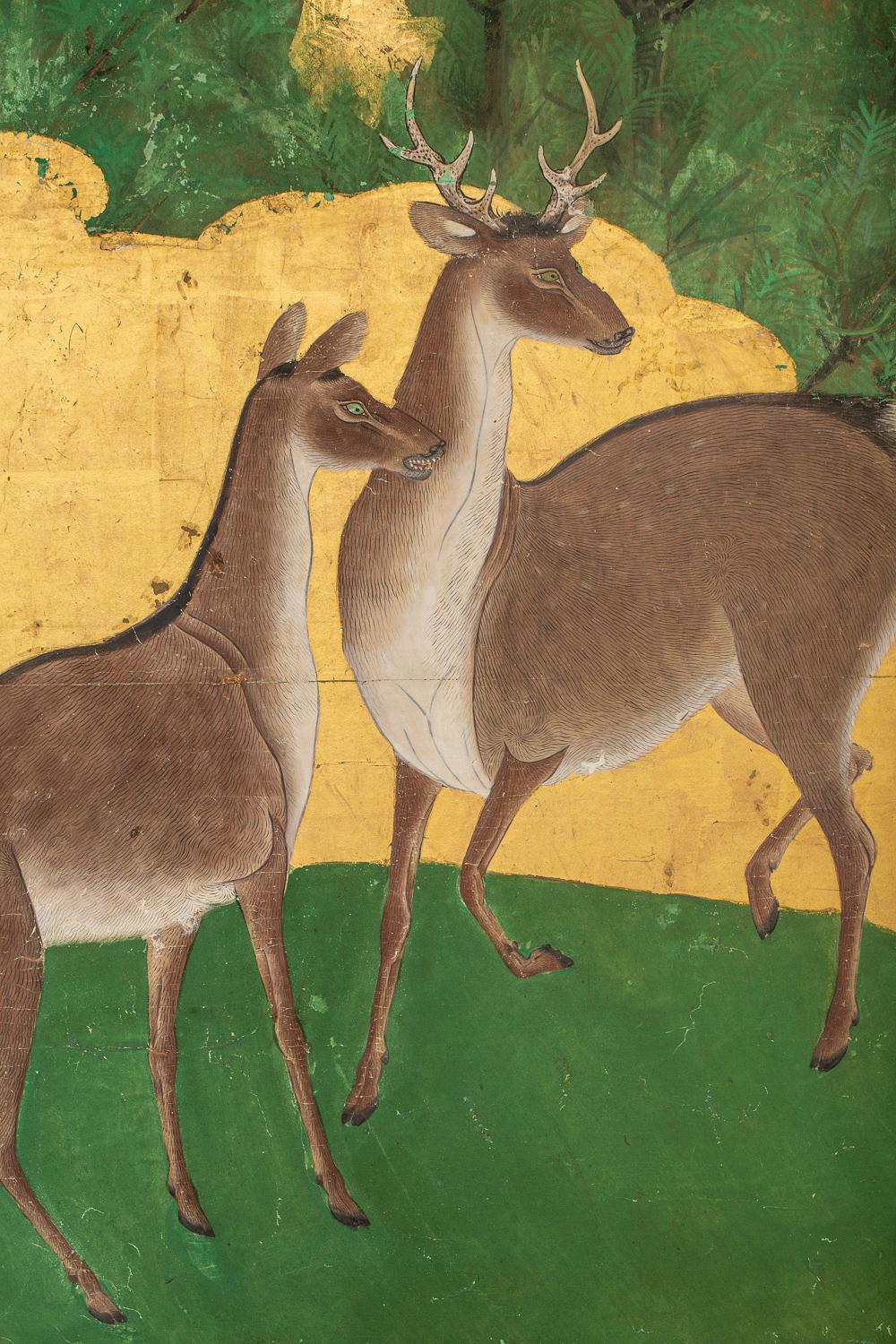 Originally fusuma doors, three deer stand in a clearing in a pine forest with gold leaf mist.  Mid Edo period painting in mineral pigments on gold leaf with a silk brocade border.