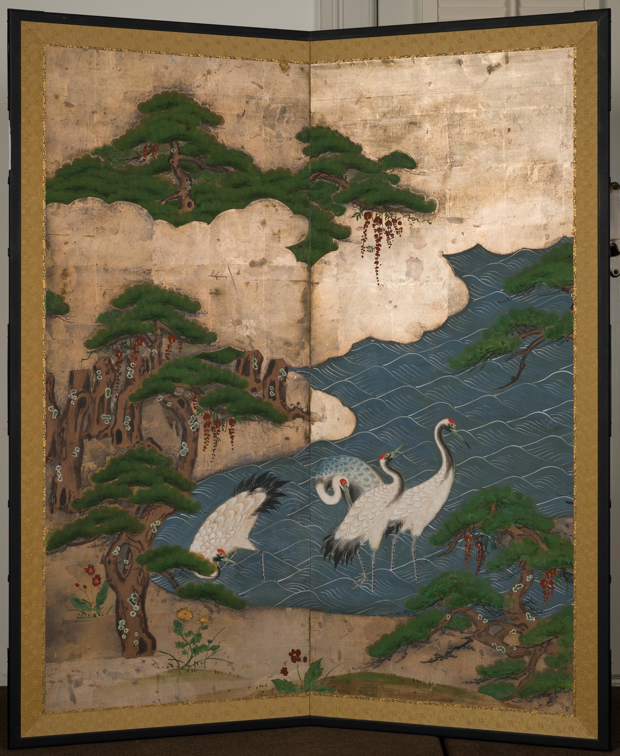Cranes wading in the water surrounded by a pine grove and silver leafs clouds.
     