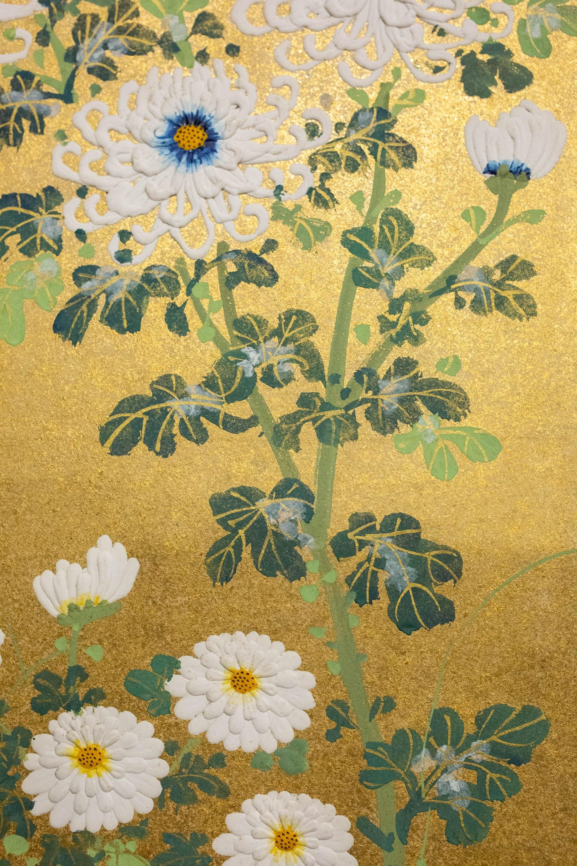 Detailed painting of varieties of chrysanthemums behind a bound-twig garden fence rendered in silvered, raised gofun. Stylized low-hanging gold mist clouds. Rimpa-style painting in mineral pigments on paper with all-over gold dust, and silk brocade