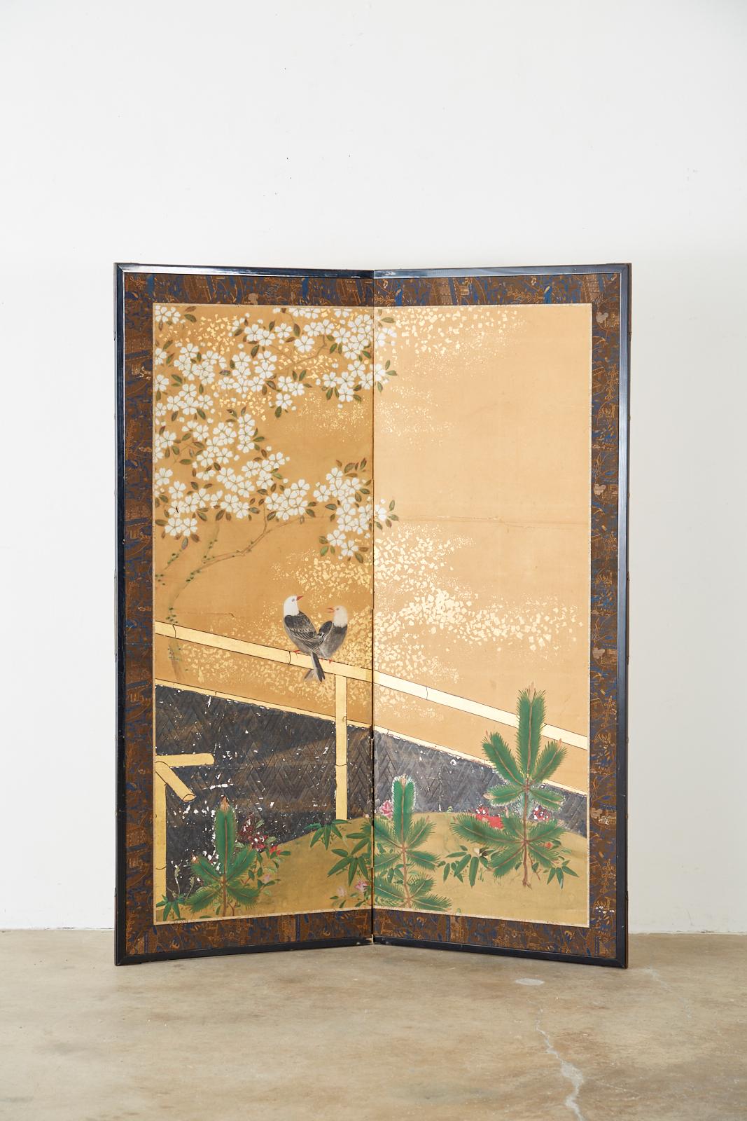 Serene Japanese two-panel Showa period screen depicting a pair of birds resting on a bamboo fence. Above the birds is a white blossoming Sakura cherry tree and bright green pine saplings below. Made in the Nihonga school style. Ink and color