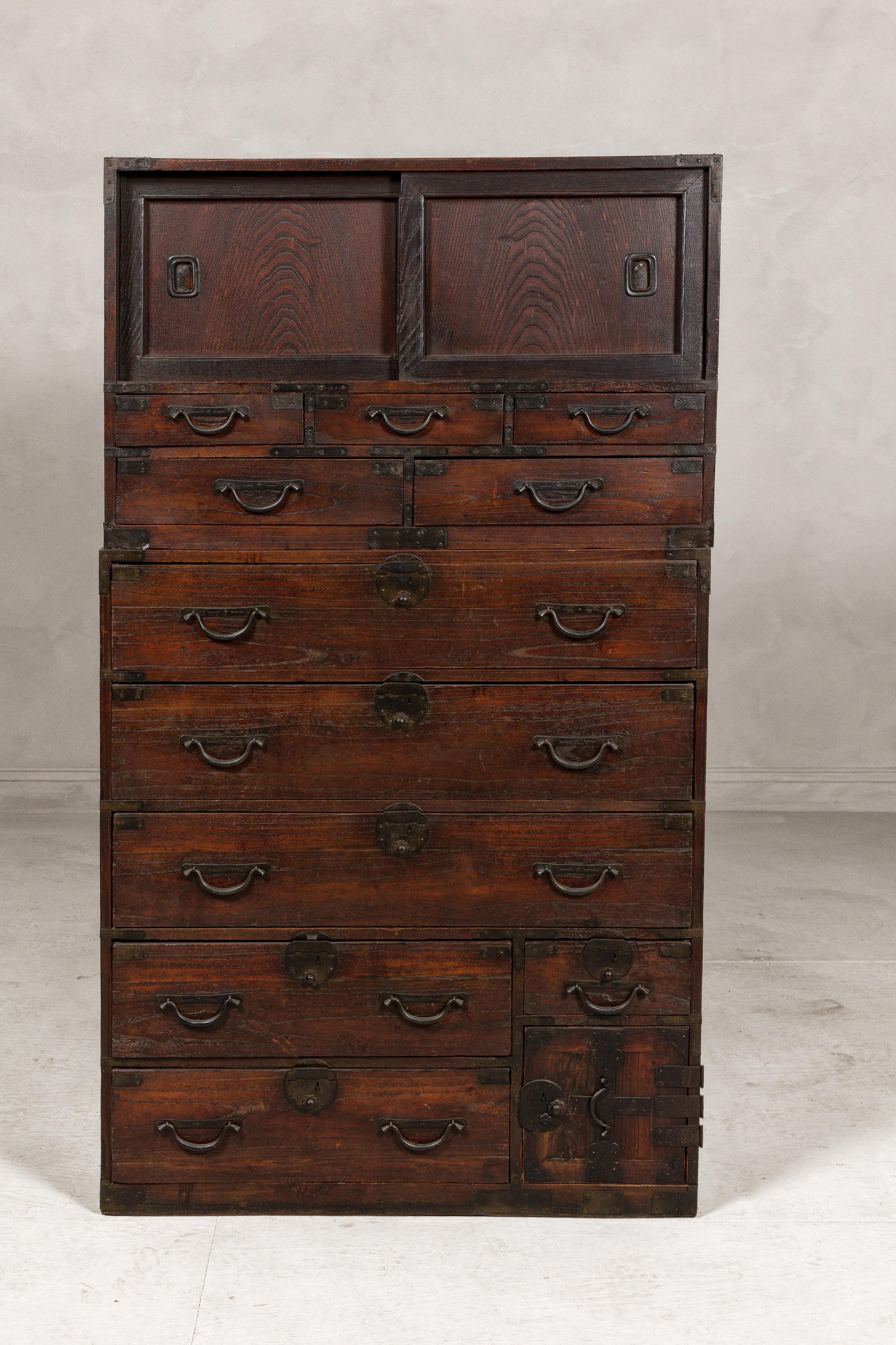 A Japanese antique two-piece Tansu chest cabinet from the 19th century with two sliding doors, 11 drawers and safe section. This 19th-century Japanese antique Tansu chest cabinet is a remarkable piece of history and craftsmanship, blending