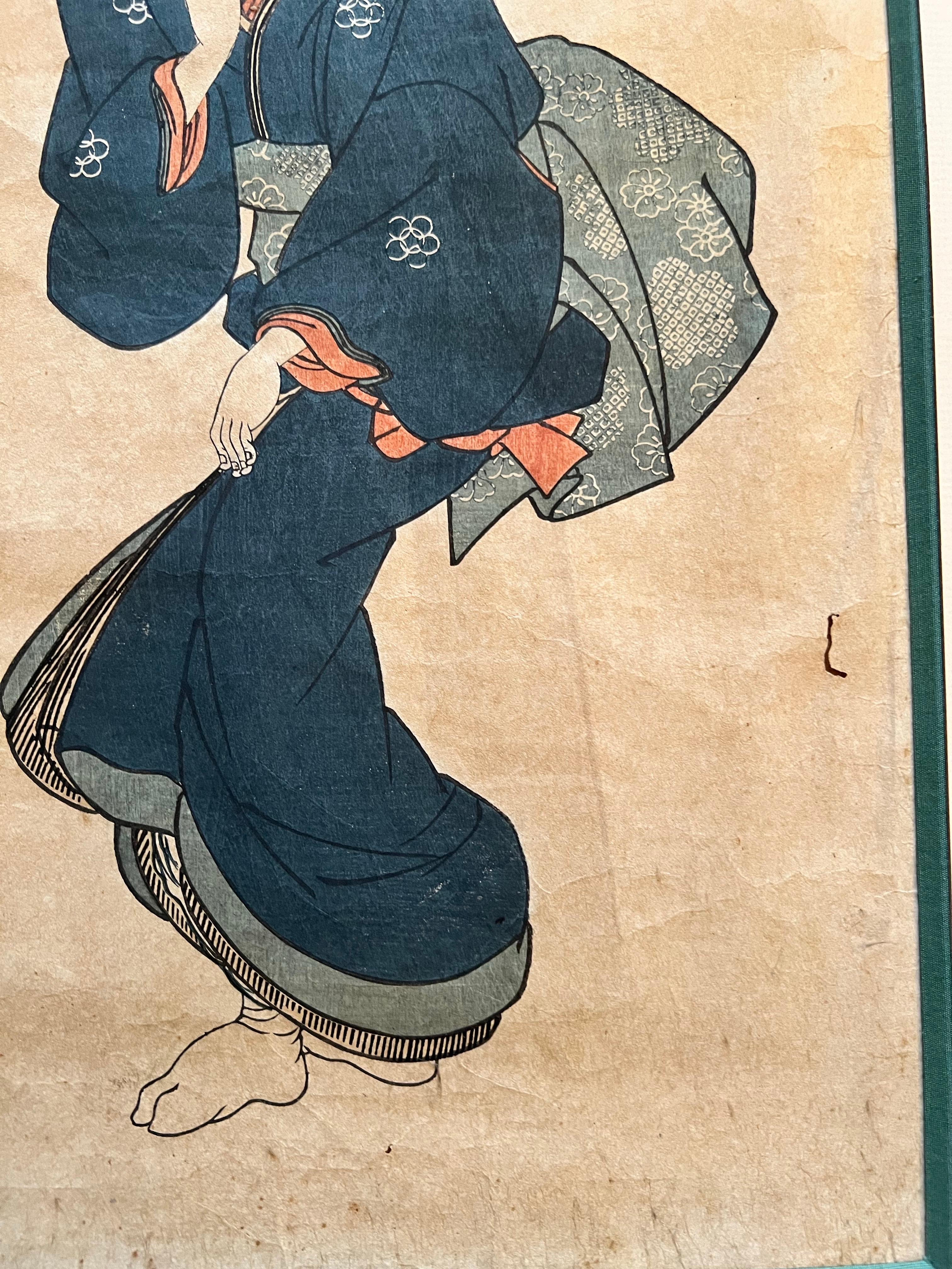 Ein prächtiger japanischer Ukiyo-e-Holzschnitt, der eine elegante junge Frau in einem blauen Kimono zeigt, die im Frühling unter Kirschblüten spazieren geht. Diese poetische und raffinierte Szene veranschaulicht perfekt die Raffinesse der
