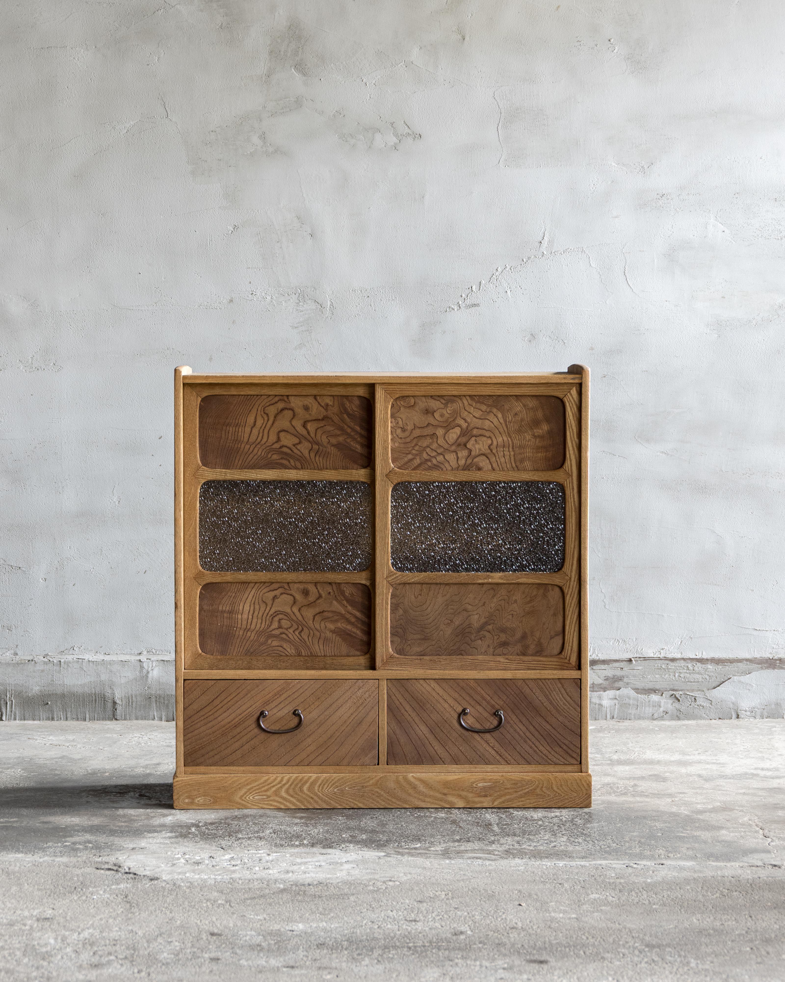 Ce meuble vintage a été fabriqué au début de la période Showa (1926-).

De taille compacte, il est construit principalement en bois japonais Sen. Les portes coulissantes associent le panneau keyaki (zelkova) au verre texturé à motif de diamant, un