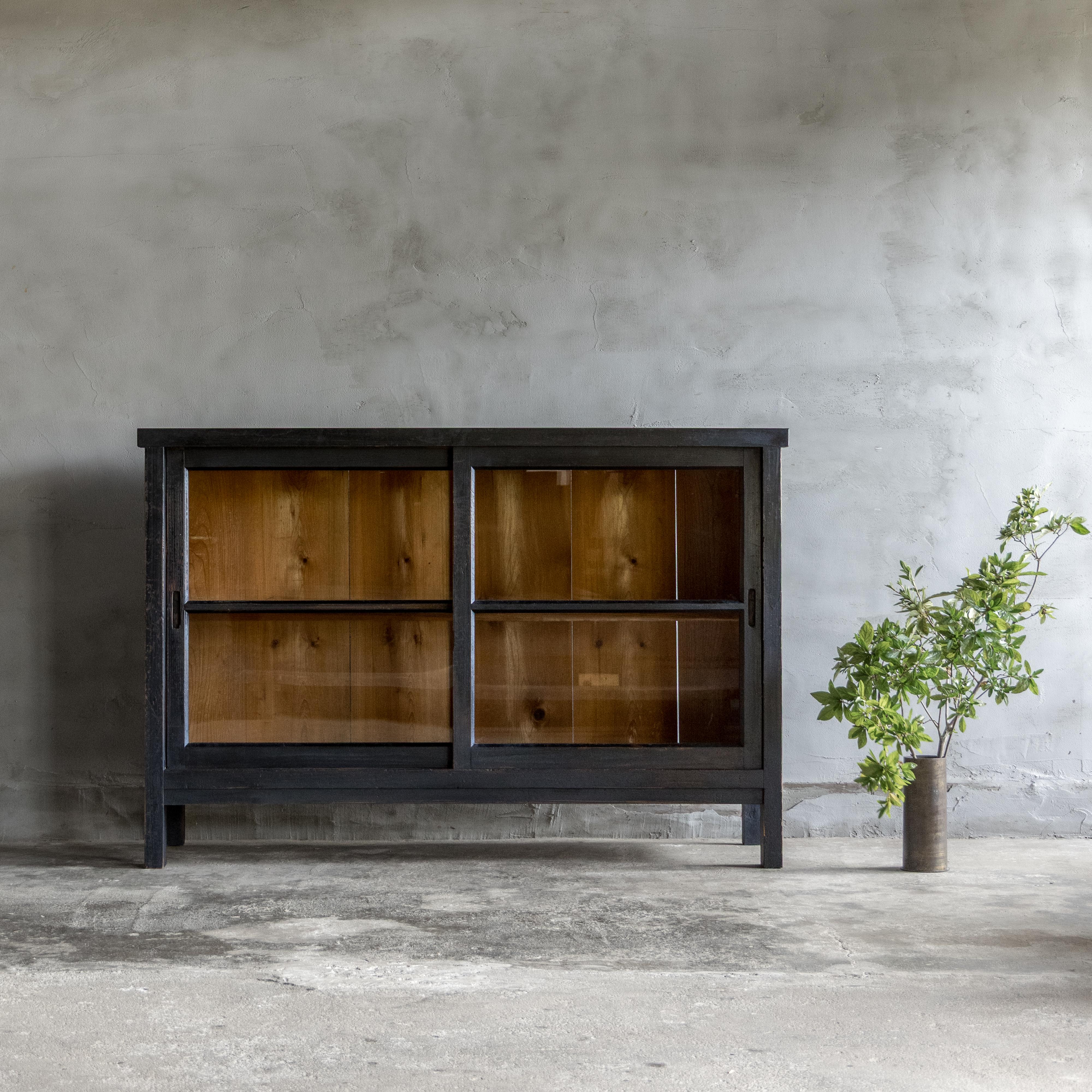 This vintage cabinet was crafted in the Early Showa Period (1926–).

Made from Japanese cedar with a black finish, the surface shows a gentle, time-worn character that adds subtle wabi-sabi charm without feeling heavy.

Behind the glass sliding