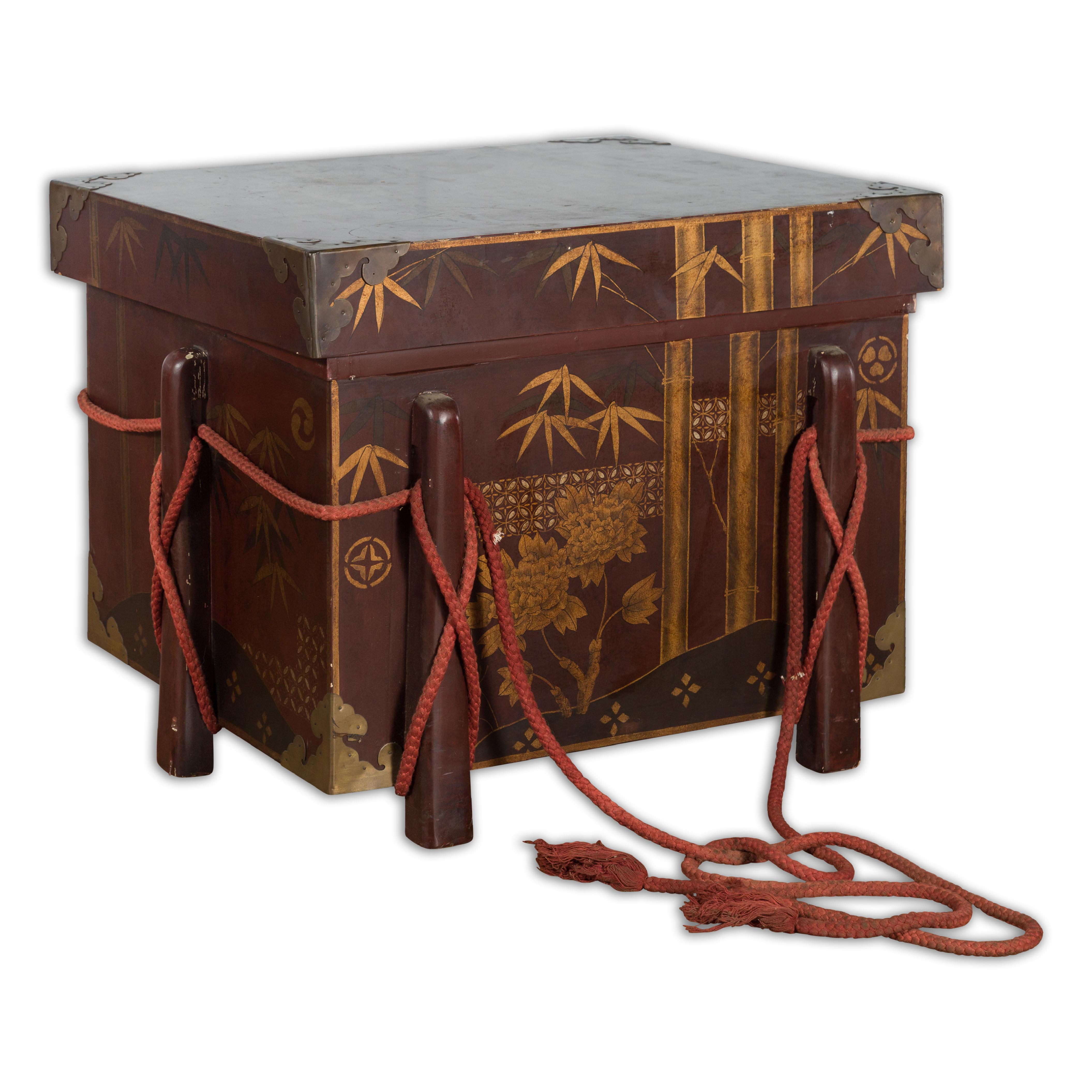 A vintage Japanese reddish brown lacquered wedding chest from the mid 20th century, with hand-painted foliage and floral décor and ropes. Created in Japan during the midcentury period, this vintage wedding box features a reddish brown lacquer