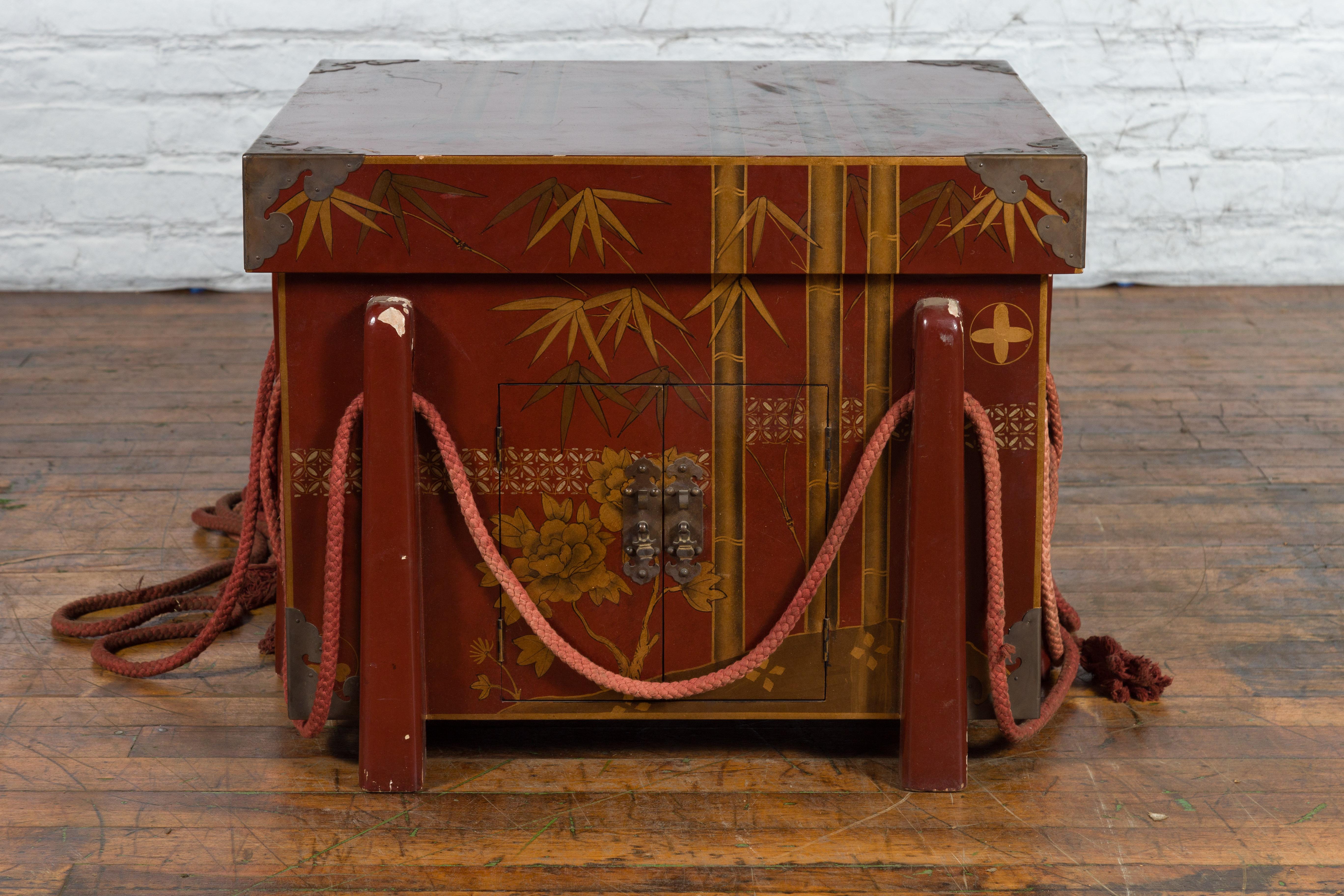 A vintage Japanese oxblood red lacquered wedding chest from the mid 20th century, with hand-painted foliage décor, two small doors and ropes. Created in Japan during the midcentury period, this vintage wedding box features an oxblood red lacquer