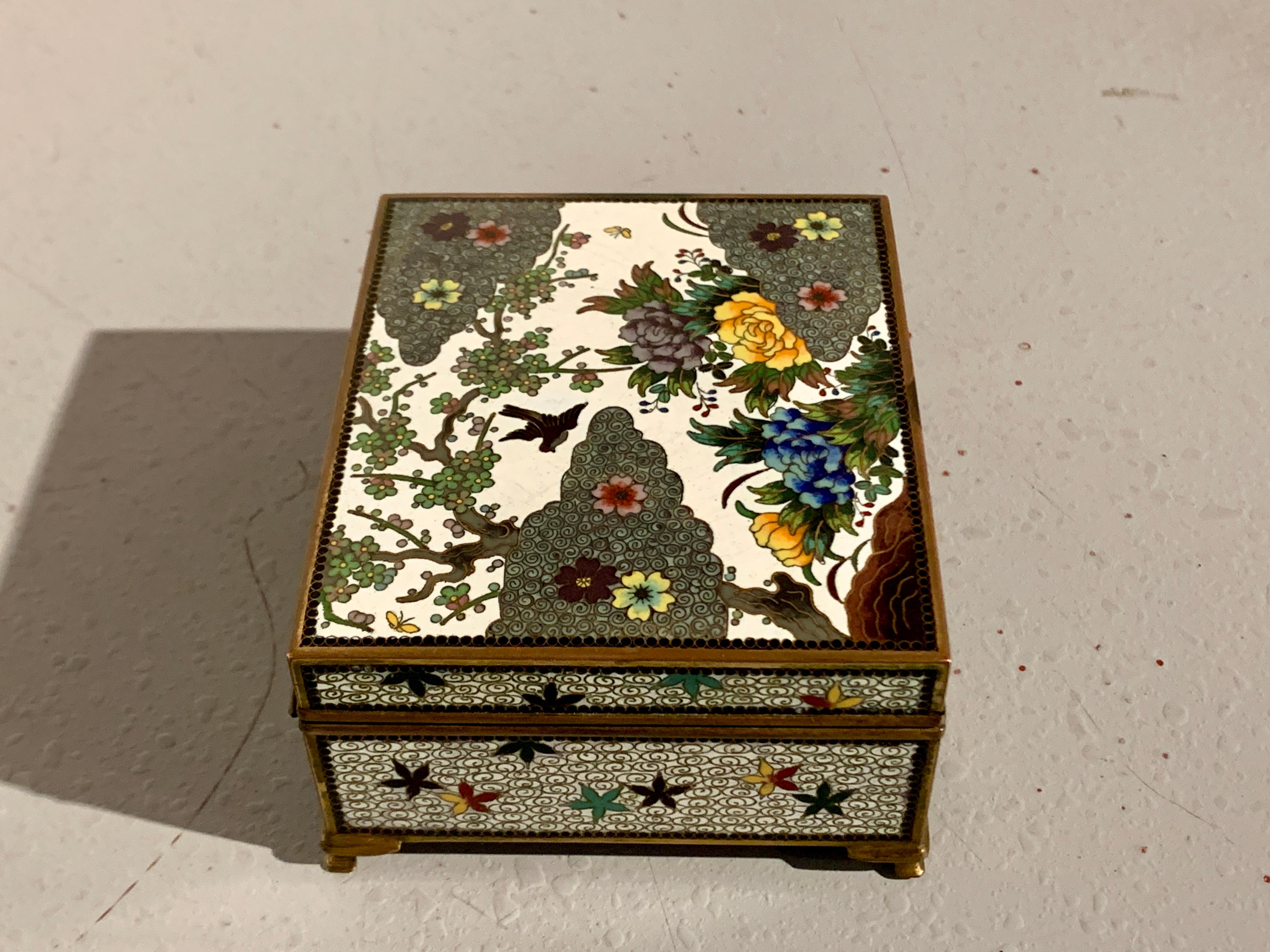 An attractive and well decorated Japanese white cloisonne hinged top box, Meiji period, circa 1910, Japan.

The small trinket or jewelry box sits on four short bracket feet. The top of the box features a pictorial scene, in a myriad of colored