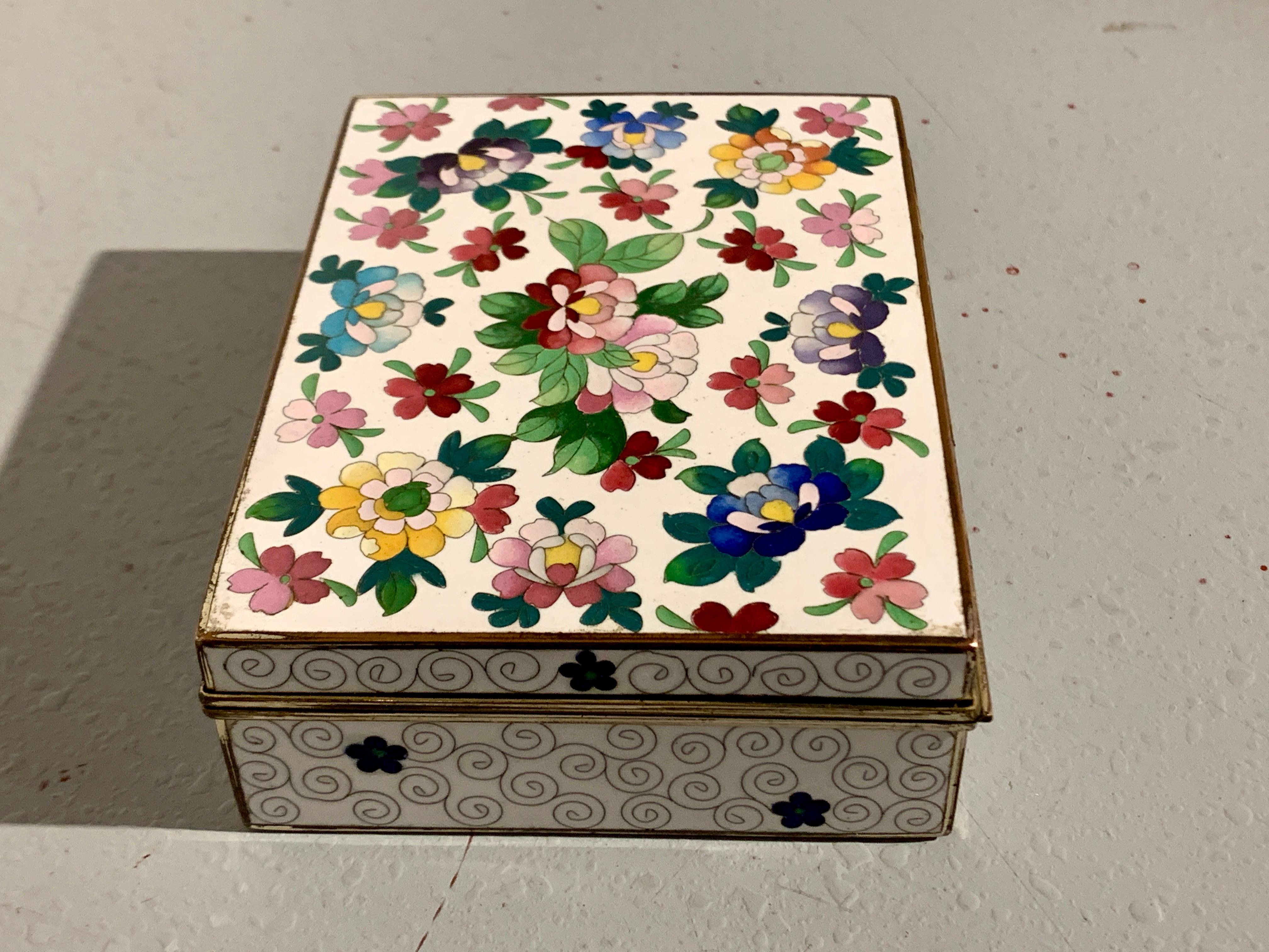 A delightful Japanese white ground cloisonne box, Showa Era, circa 1930's, Japan.

The trinket or keepsake box with a fanciful floral design to the hinged top. The flowers in shades of blues, plurals, reds, yellow, and pinks surrounded by green