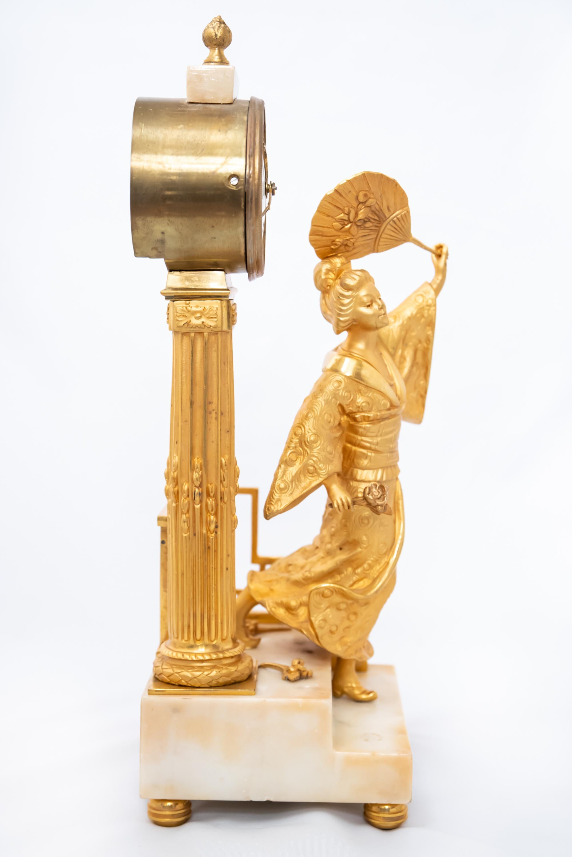 A French fire-gilt bronze clock with marble base depicting a Japanese woman, Louis XVI or Empire Era, 1790-1815. The silk-thread mechanism is in good working condition with key and pendulum.
