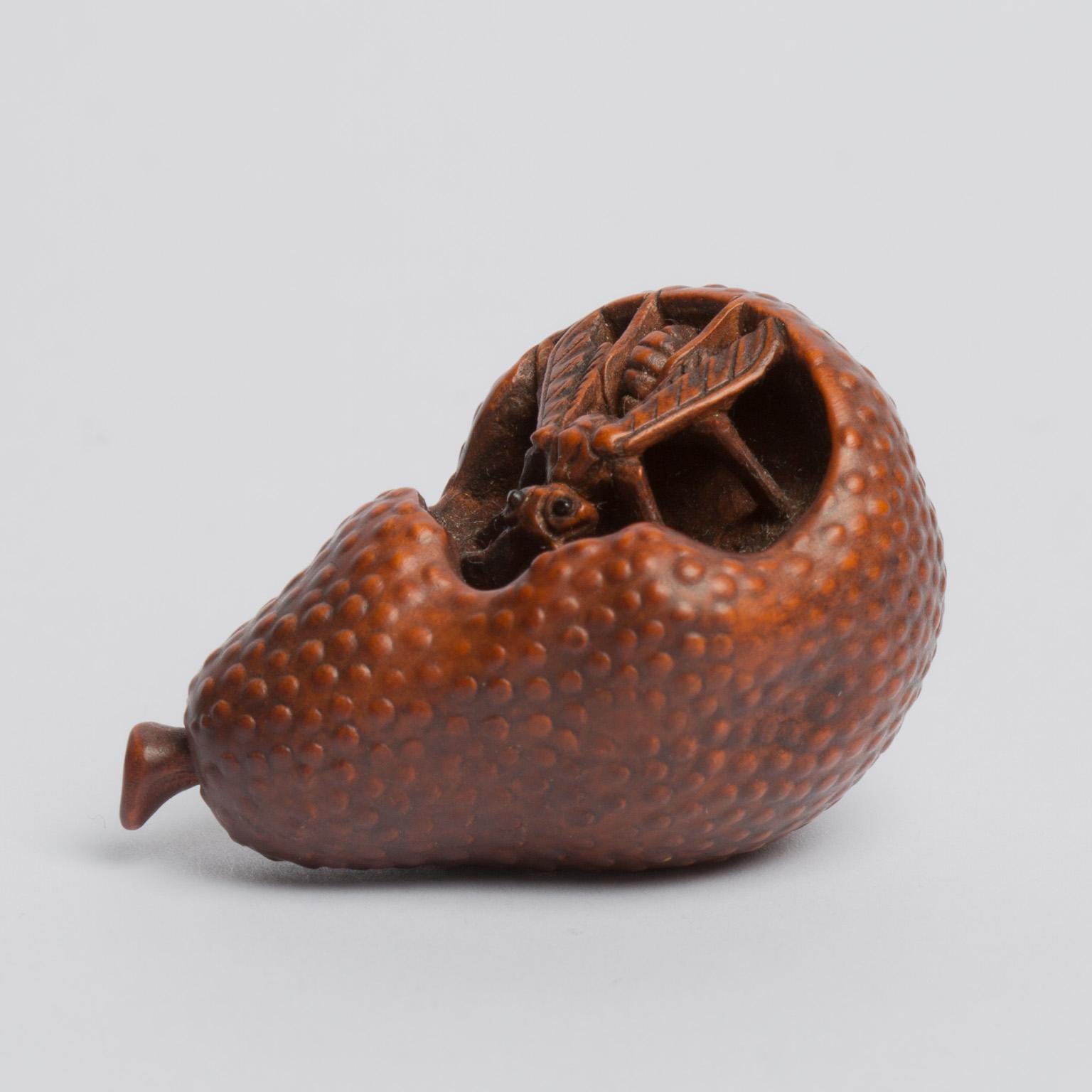 A fine wood netsuke of a wasp feeding on the rotting flesh of a pear, the rough texture of the skin of the fruit rendered with little pimples in ukibori. The netuske is unsigned, but can be attributed confidently to Kogetsu. Kogetsu is the most