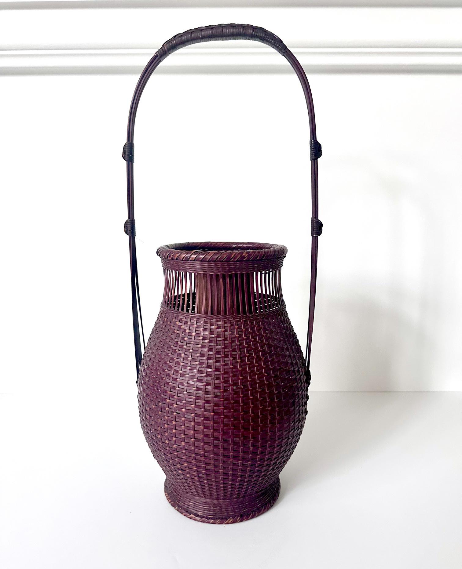 A lovely Ikebana bamboo basket hand-woven by Japanese artist Chikusie Watanabe (1932-) circa late 20th century. The Hanakago basket is of a classic vase form with elongated handle and equipped with an insert fashioned out of bamboo stalk. The